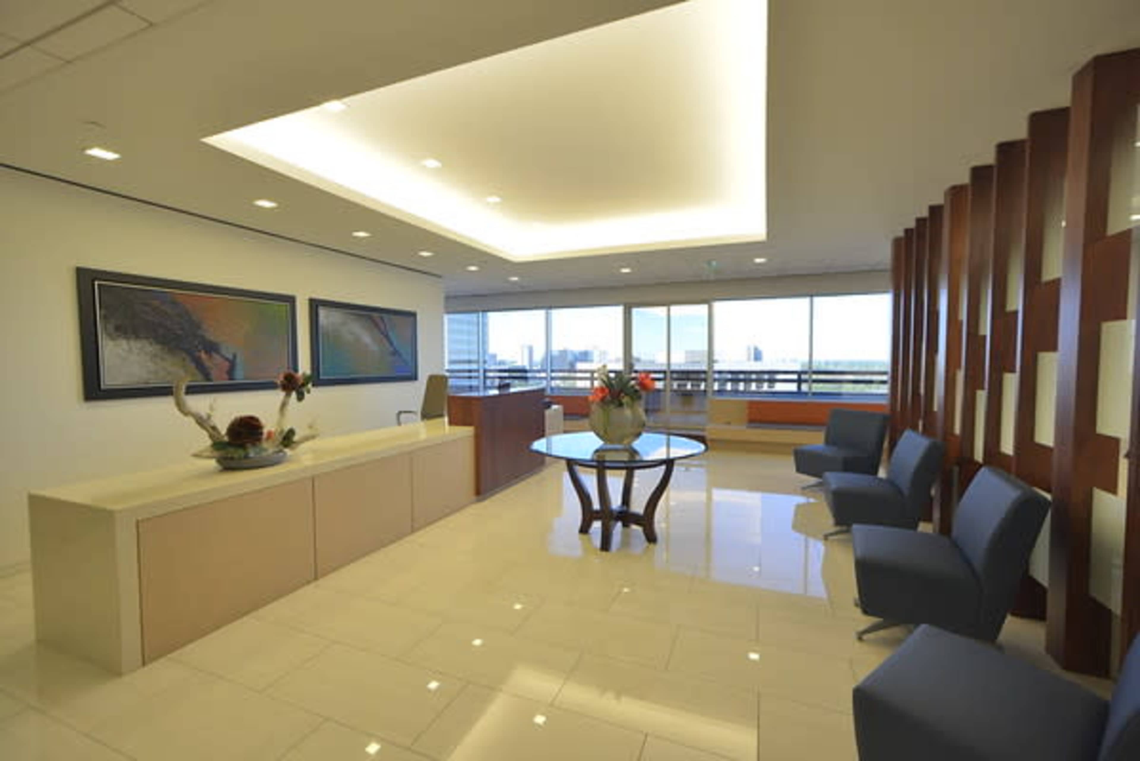 A modern office reception area with a front desk, a round table, and large windows overlooking a cityscape.