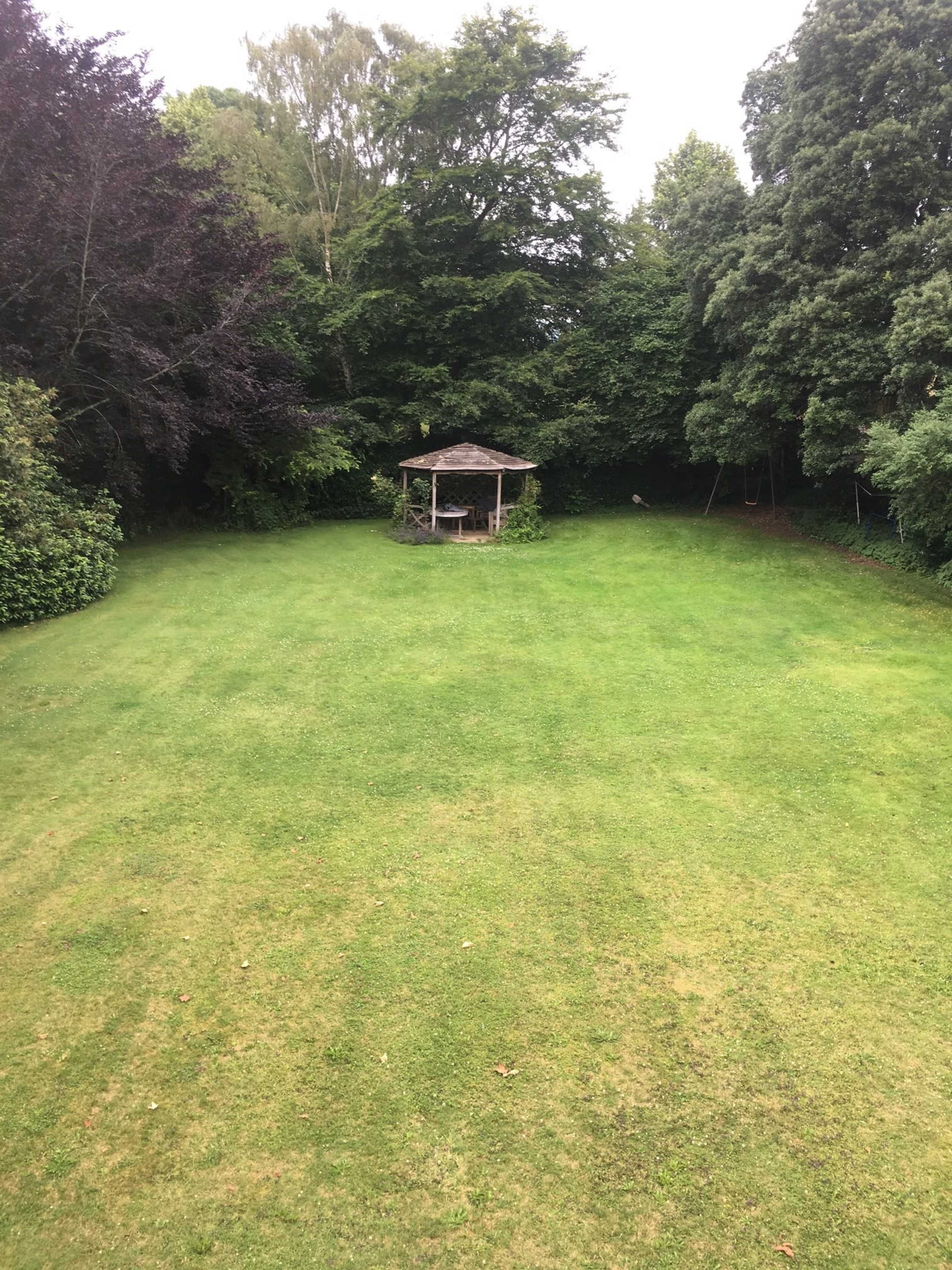 A spacious green lawn with a gazebo surrounded by trees in the background.