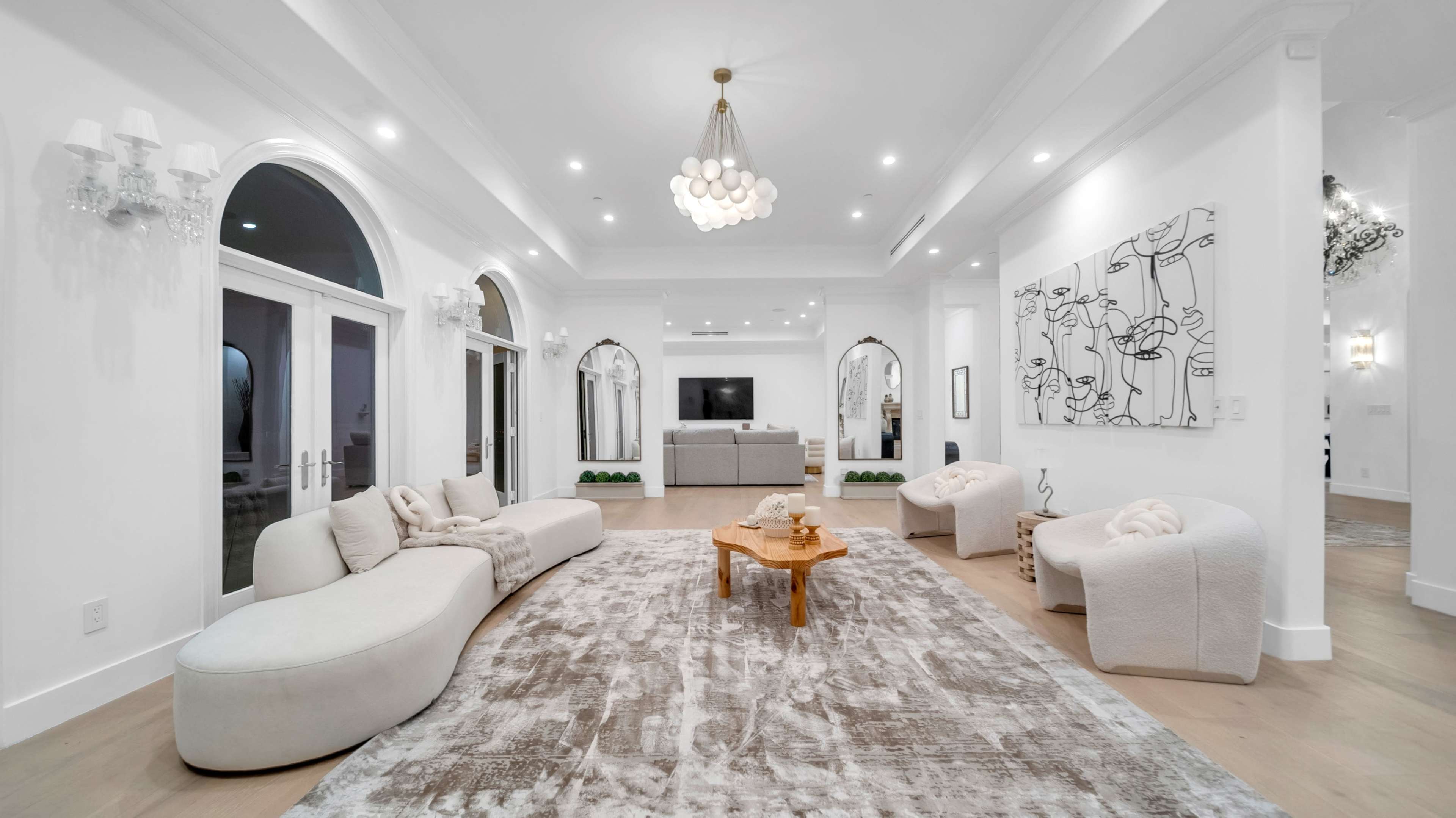 The image shows a spacious, modern living room featuring a large area rug, curved sofas, a wooden coffee table, and a neutral color palette.