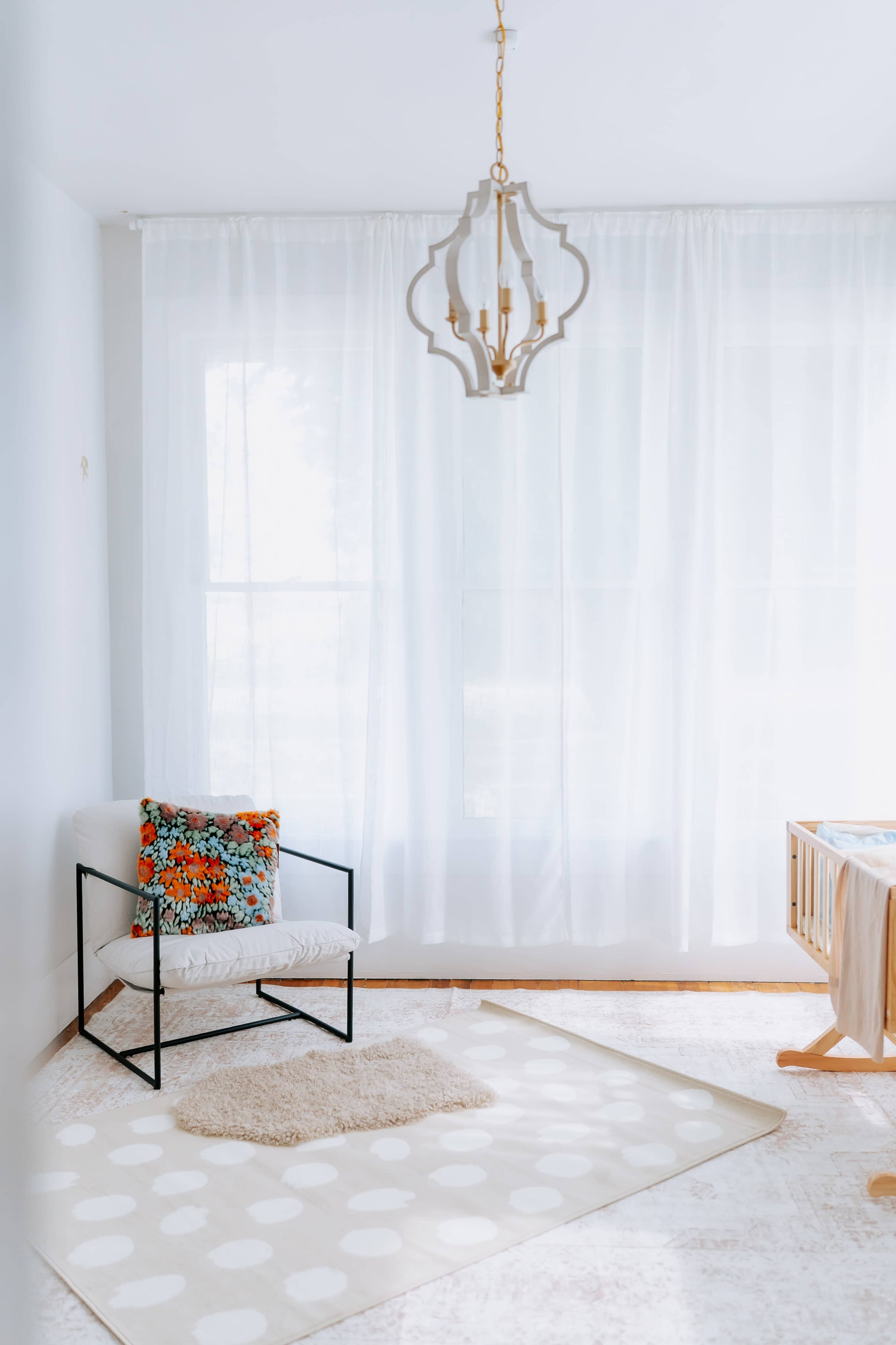 A softly lit nursery features a white armchair with a colorful cushion, next to a crib, set on a patterned rug with large polka dots.