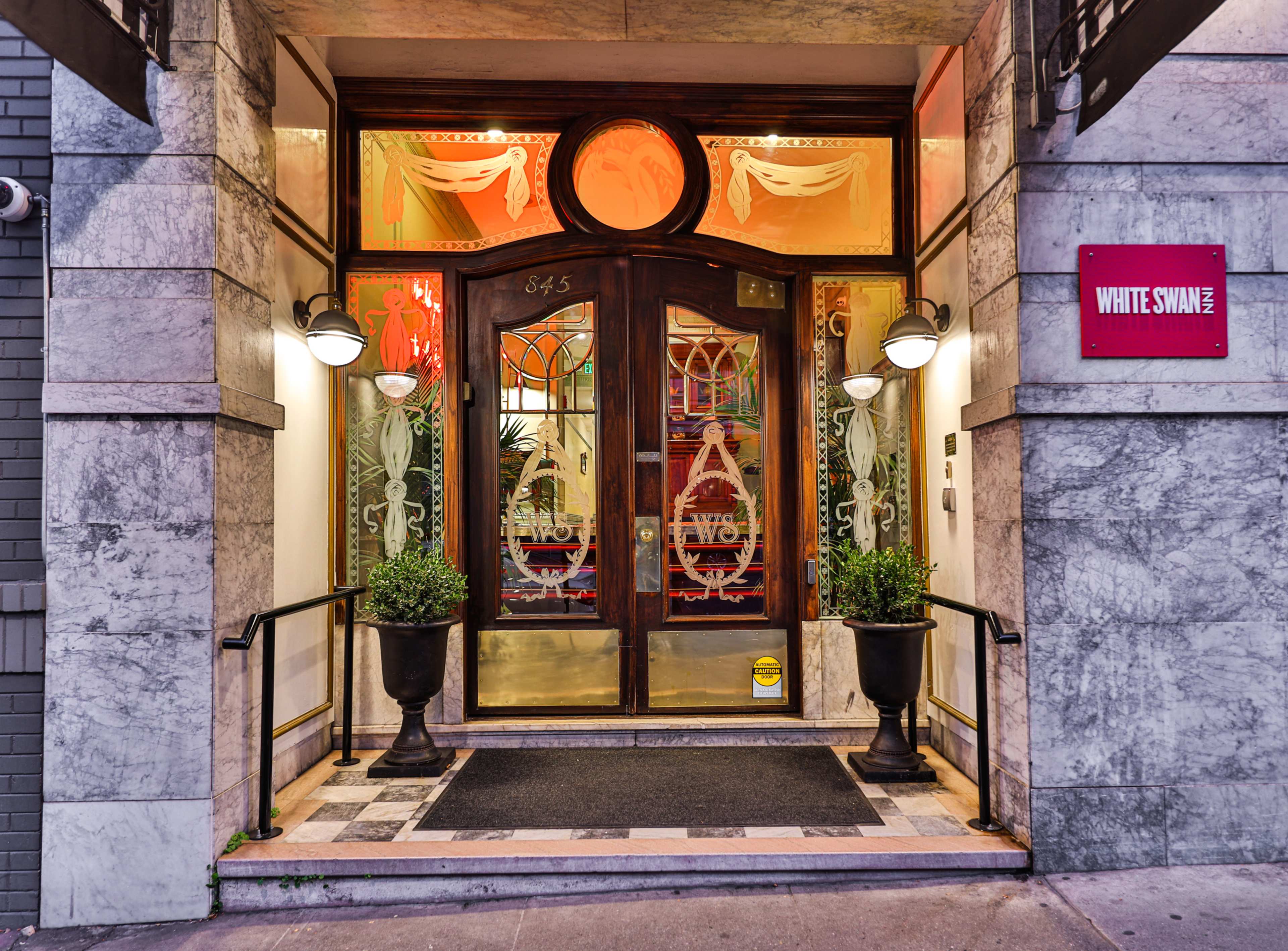 The entrance of the White Swan building features a wooden double door framed by decorative glass panels and potted plants on either side.