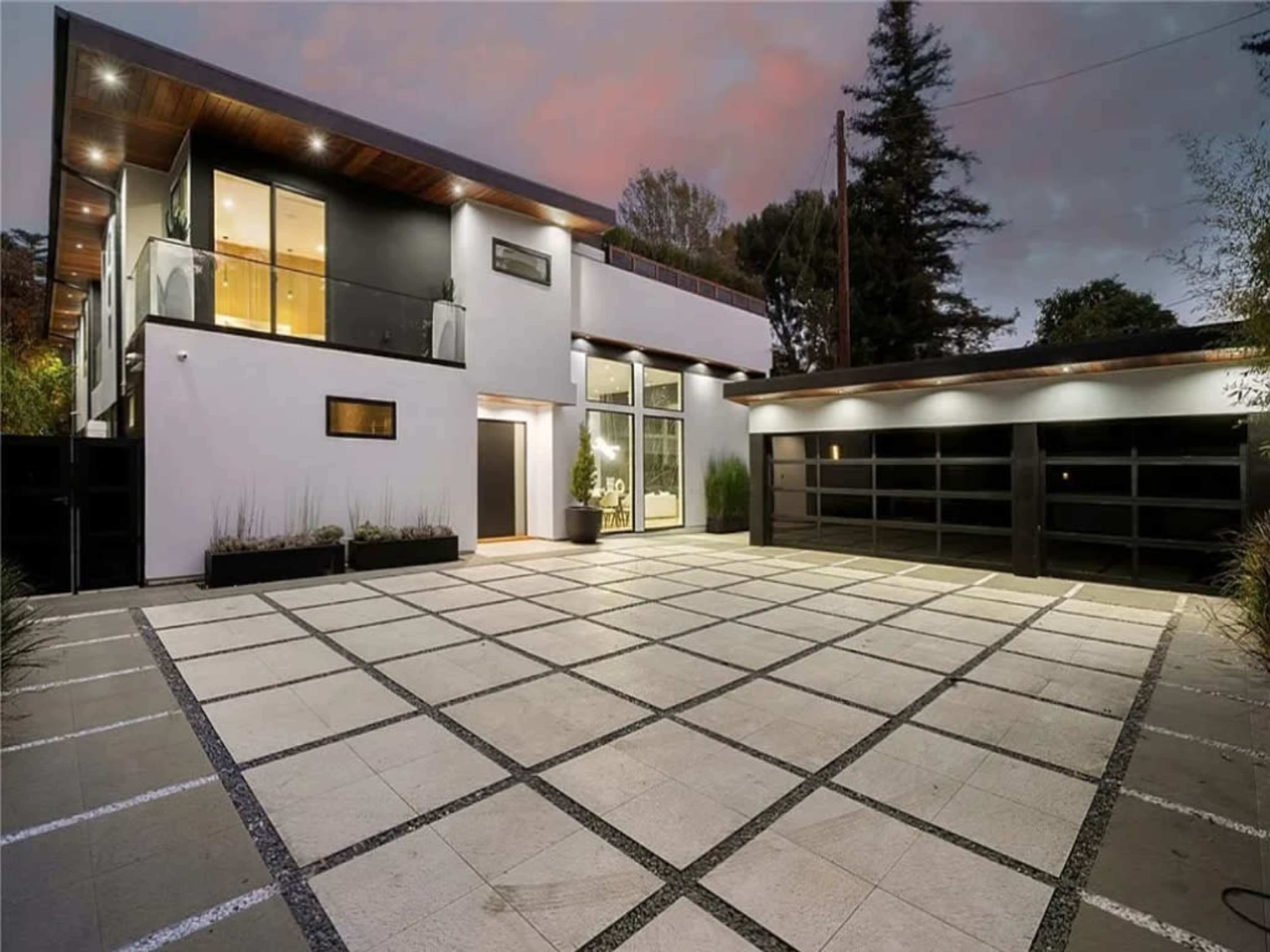 The image features a modern two-story home with a spacious driveway, large windows, and a minimalist design.
