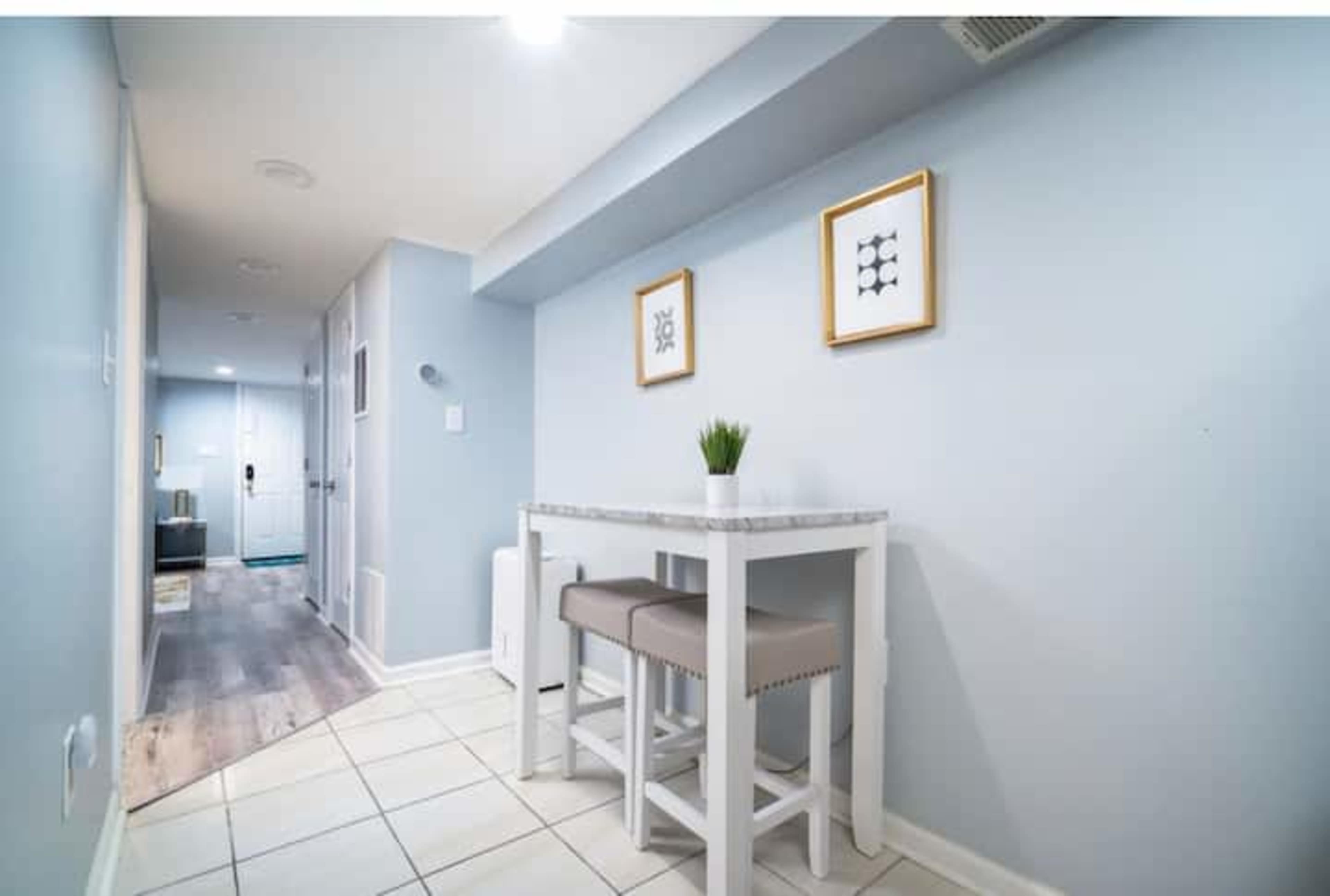 A narrow hallway features a small table with two stools and framed artwork on the walls.