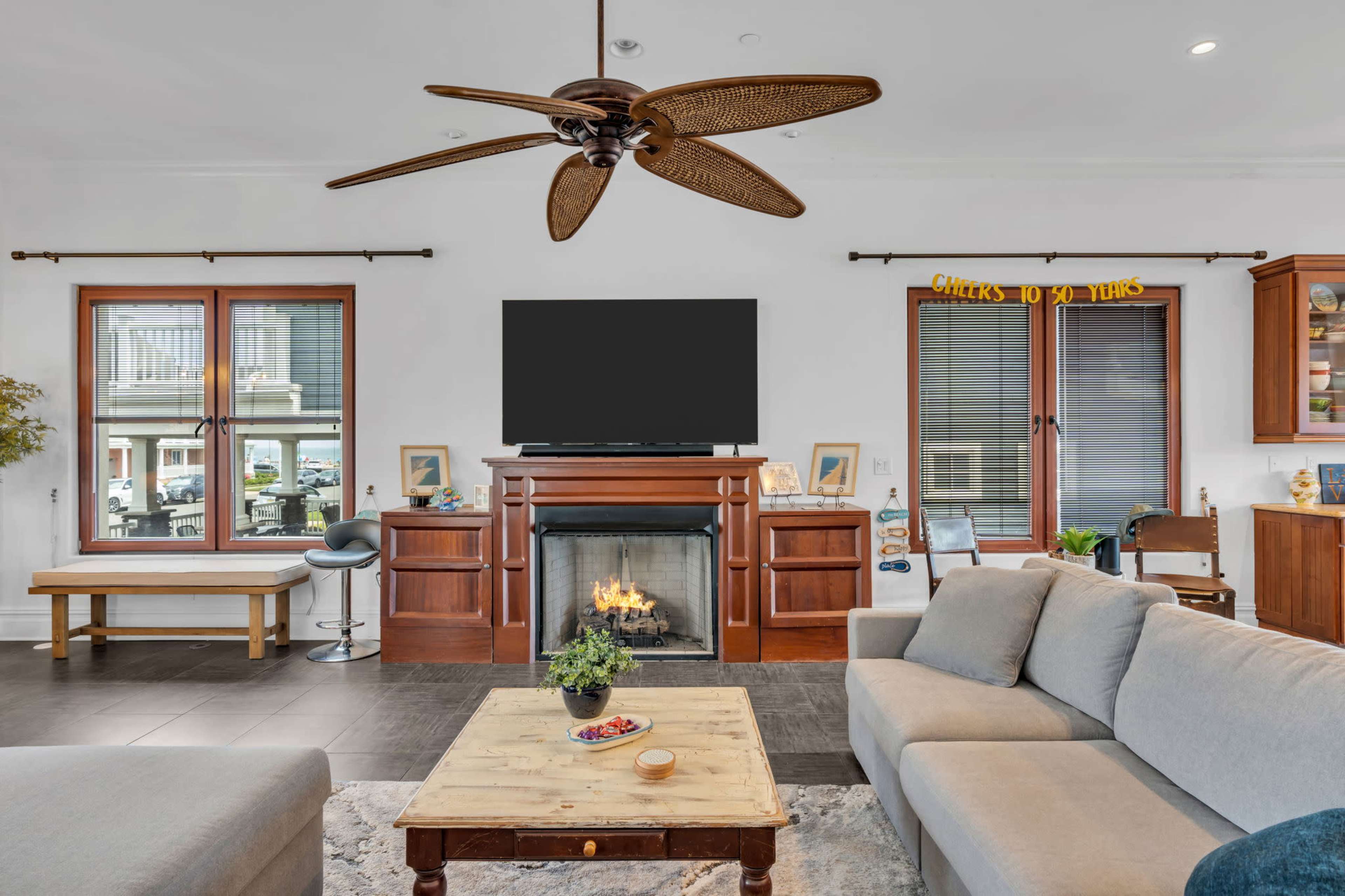 The image shows a modern living room with a ceiling fan, a TV mounted above a fireplace, and a coffee table in front of a sofa.