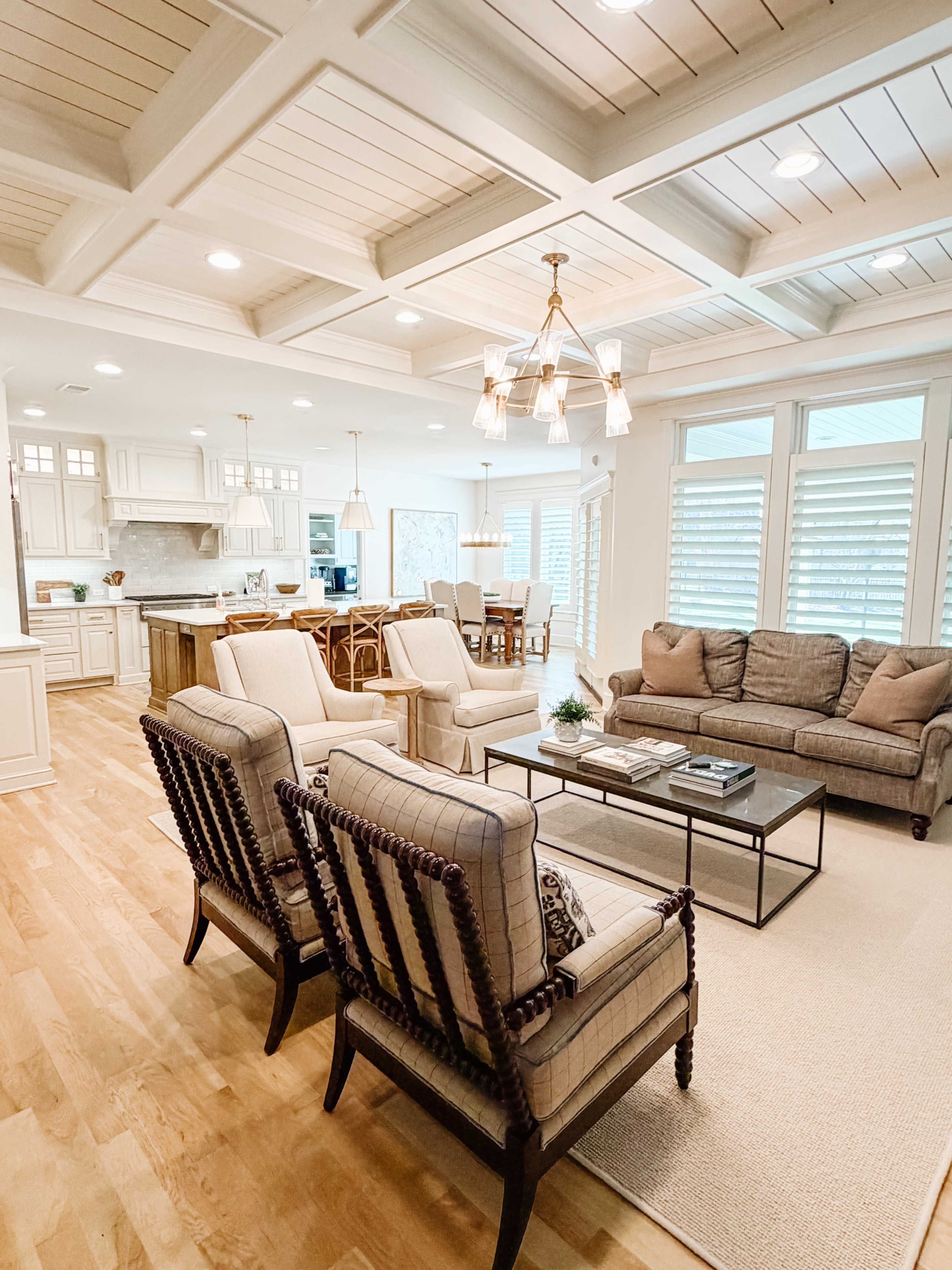 A modern living room features two patterned armchairs and a sofa, with a coffee table in the center, surrounded by a dining area and a kitchen in an open layout.