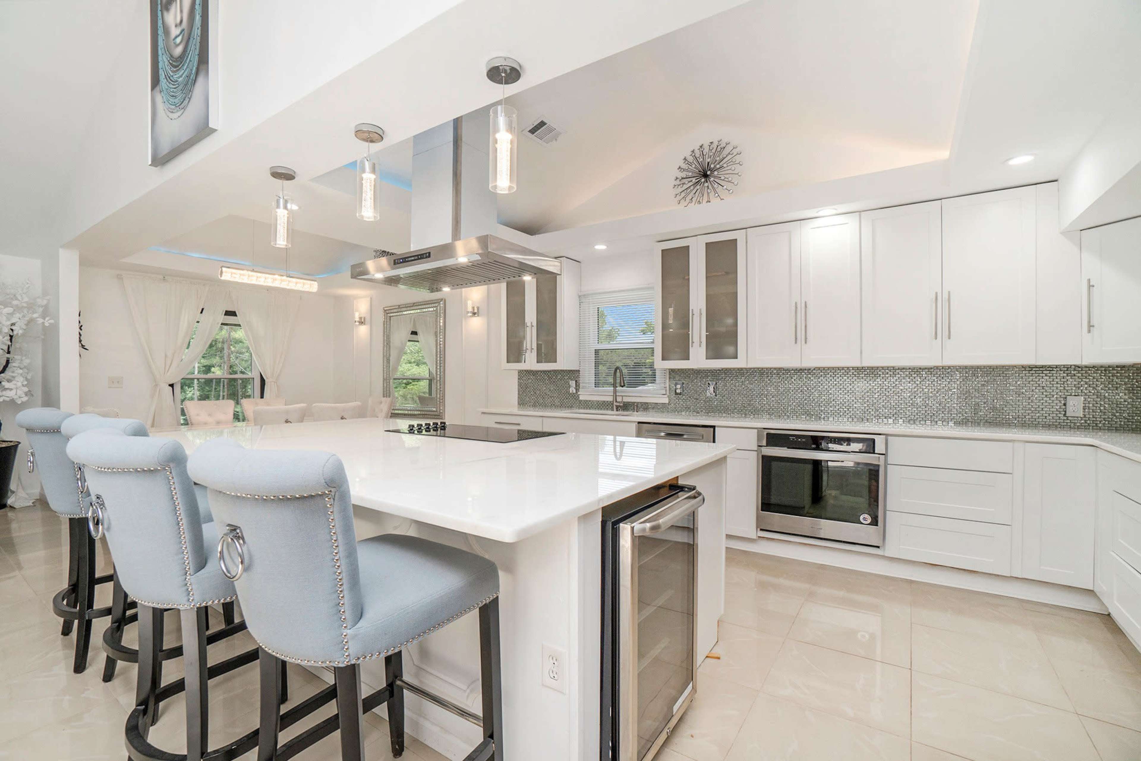 The image shows a modern kitchen with white cabinetry, a large island with bar seating, and stainless steel appliances.