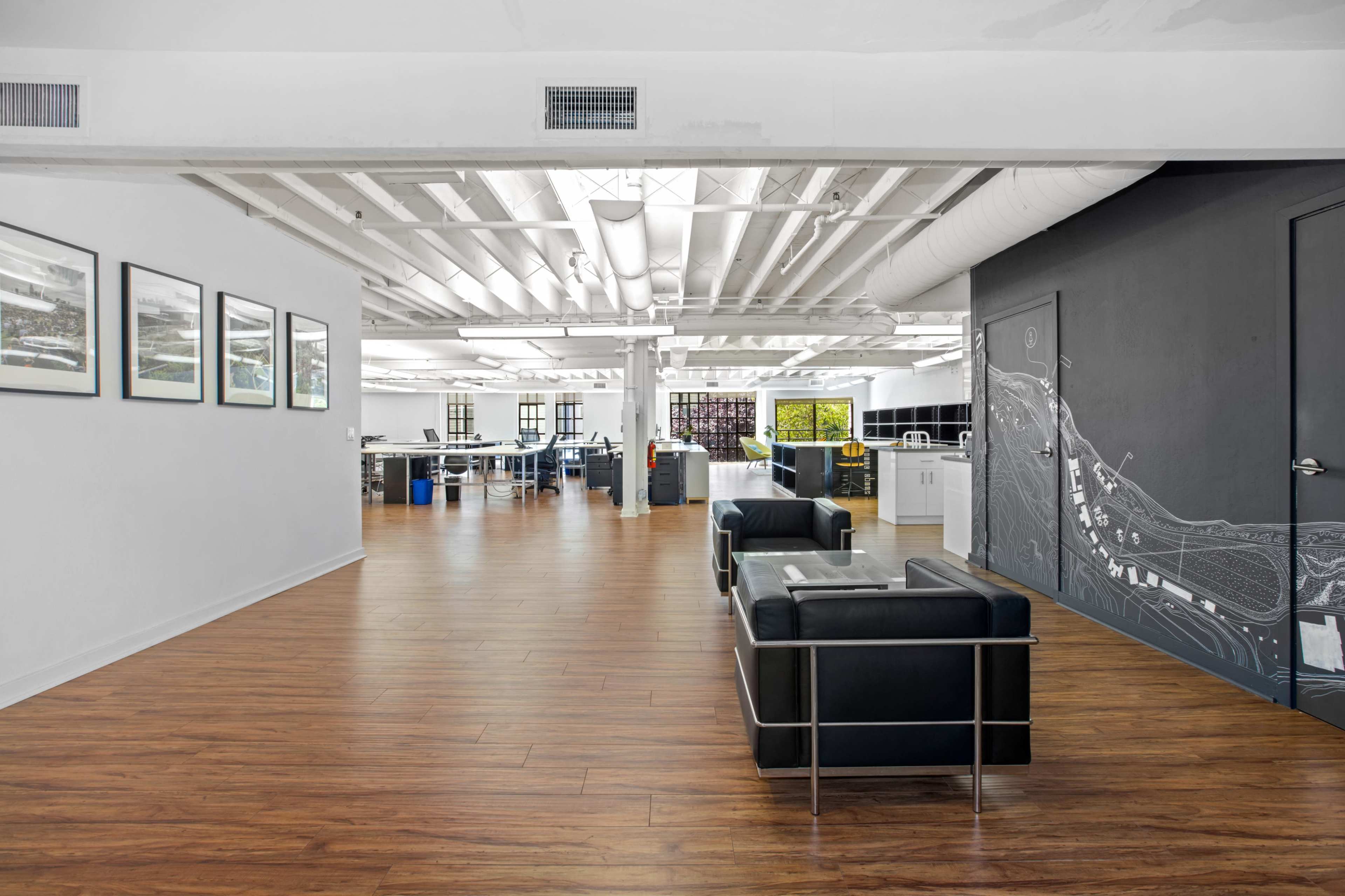 A spacious, modern office area with hardwood floors, sleek furniture, and large windows.