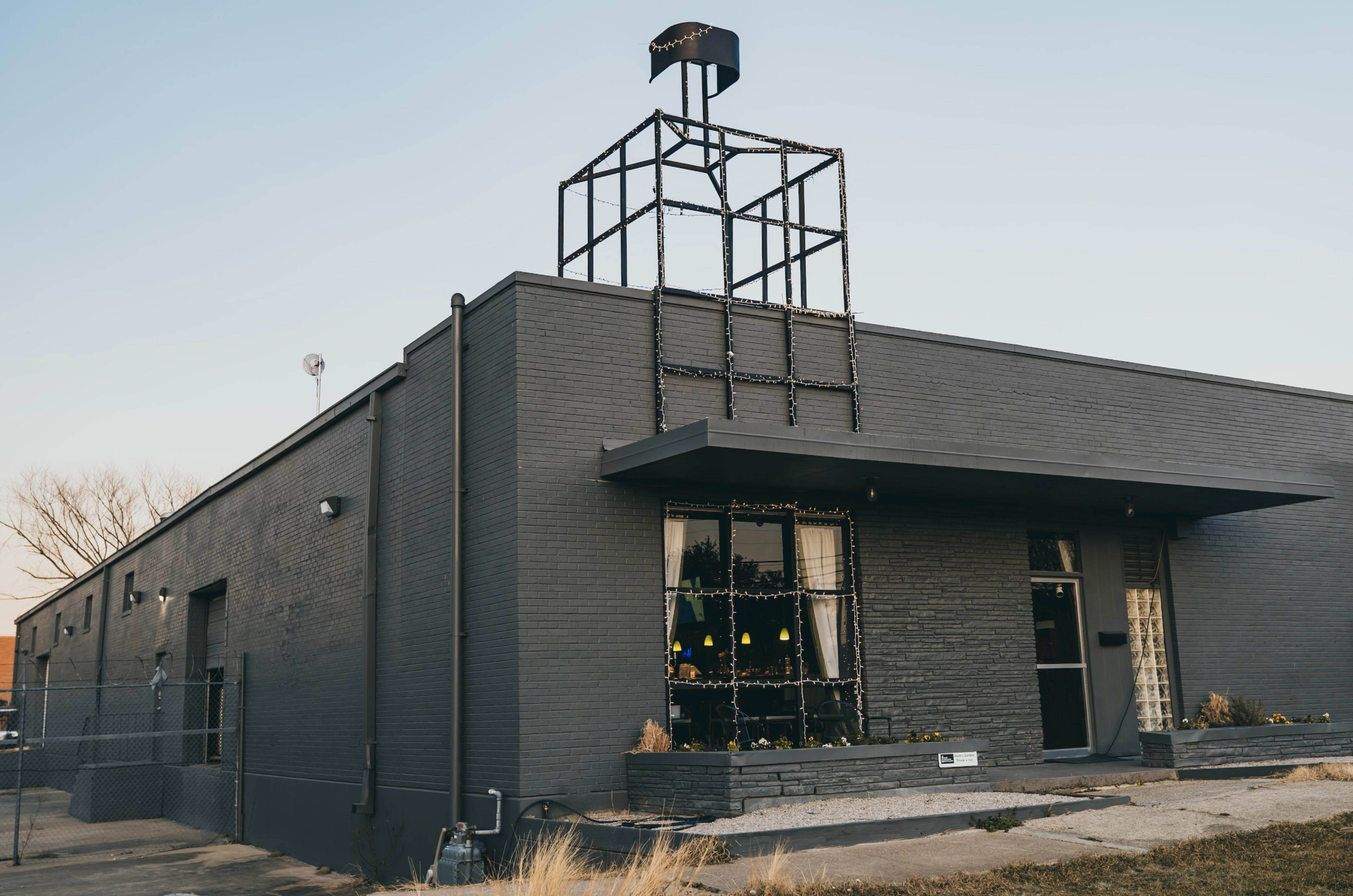 A gray building features a simple geometric structure decorated with lights on its roof and large windows framed by curtains.