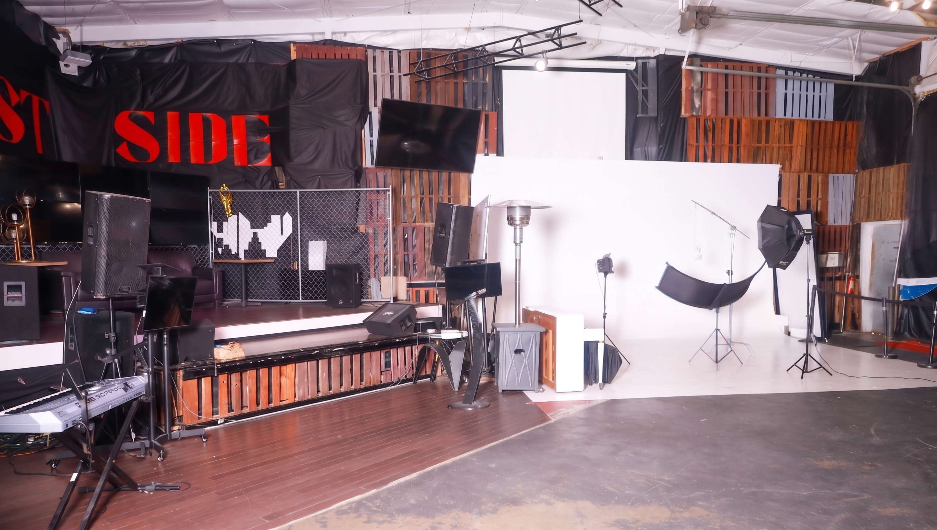 The image shows a well-lit photography studio featuring various equipment, including lighting setups, a blank backdrop, and a music keyboard against a backdrop of wooden panels.