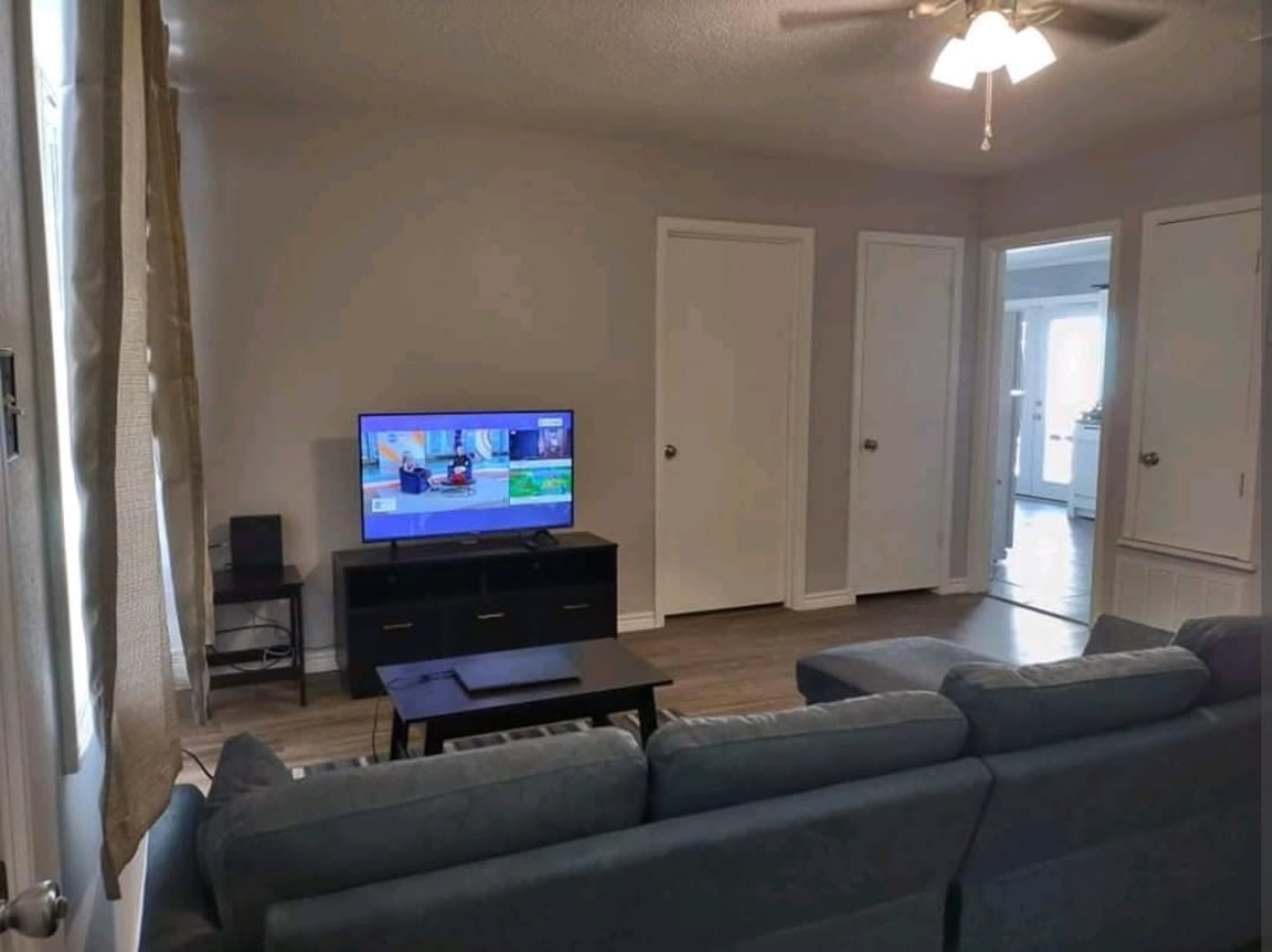 A living room features a gray couch facing a television, with two closed doors and a light fixture overhead.
