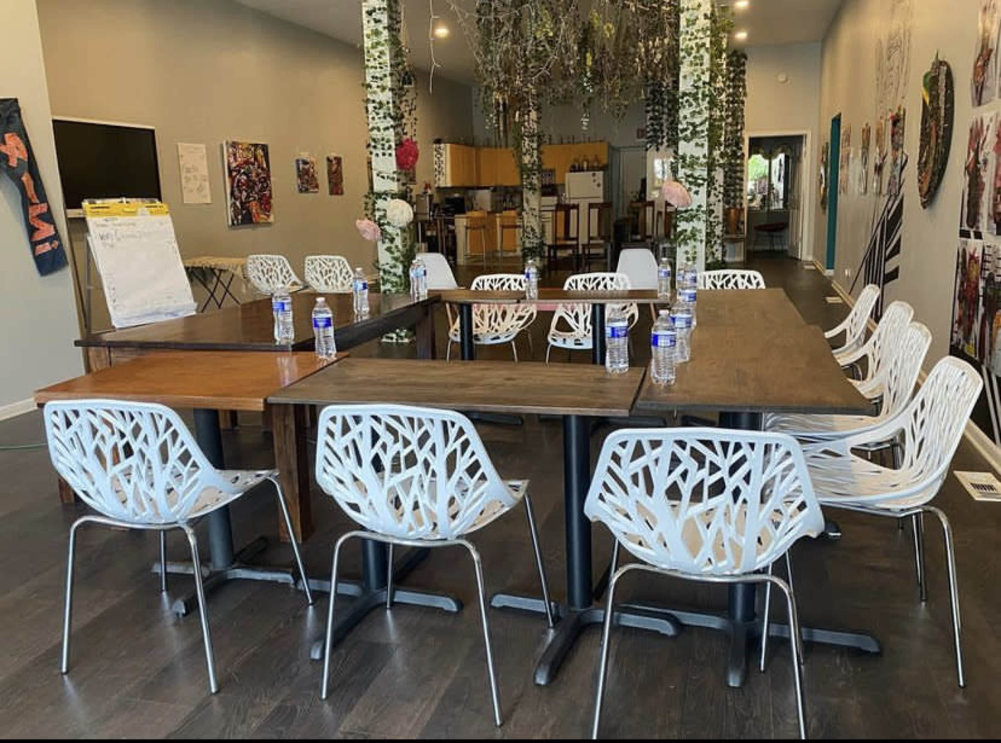 A spacious meeting room features two large tables arranged in a U-shape, surrounded by modern white chairs, with water bottles placed at each seat.