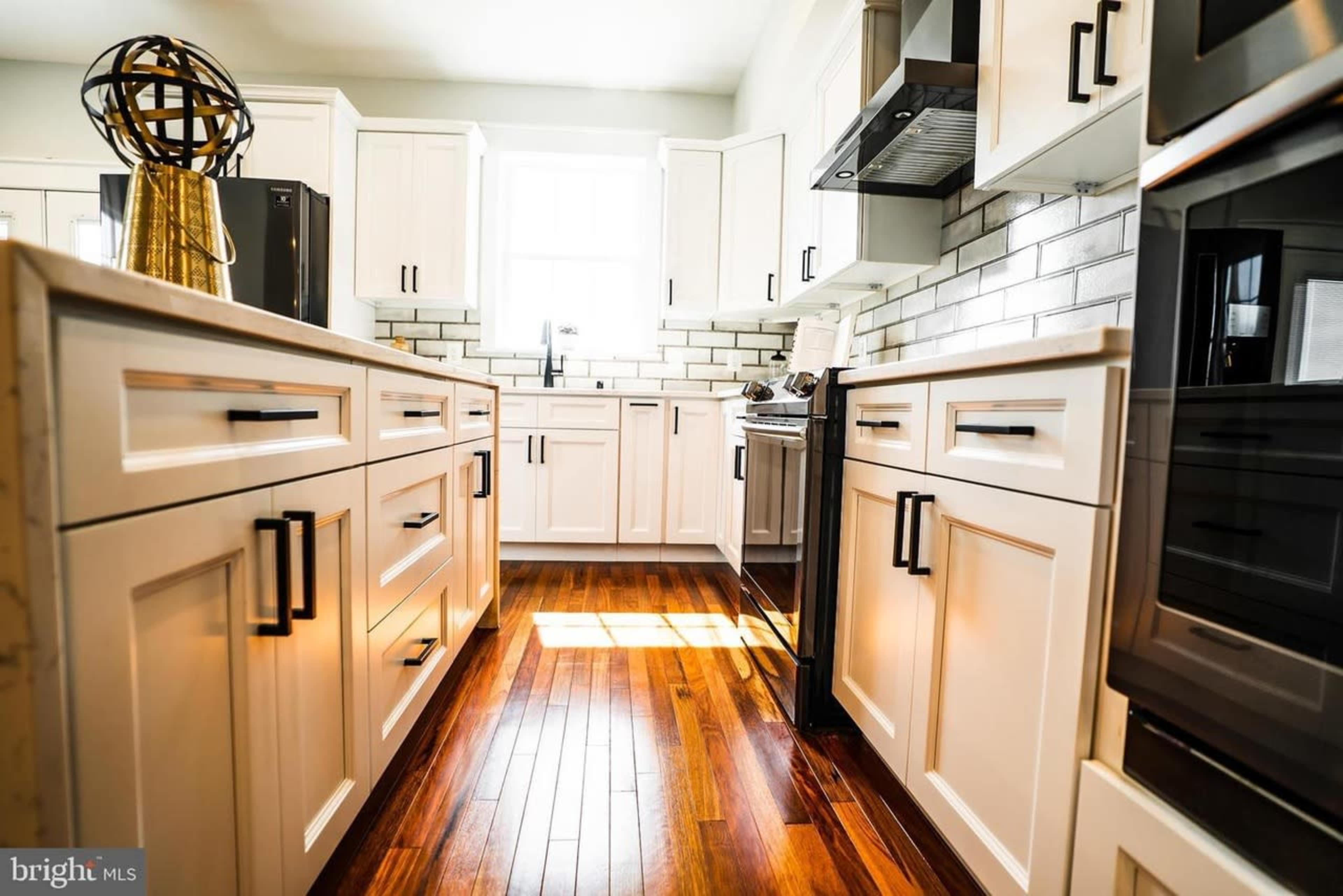 The image shows a modern kitchen with white cabinetry, stainless steel appliances, and wooden flooring.