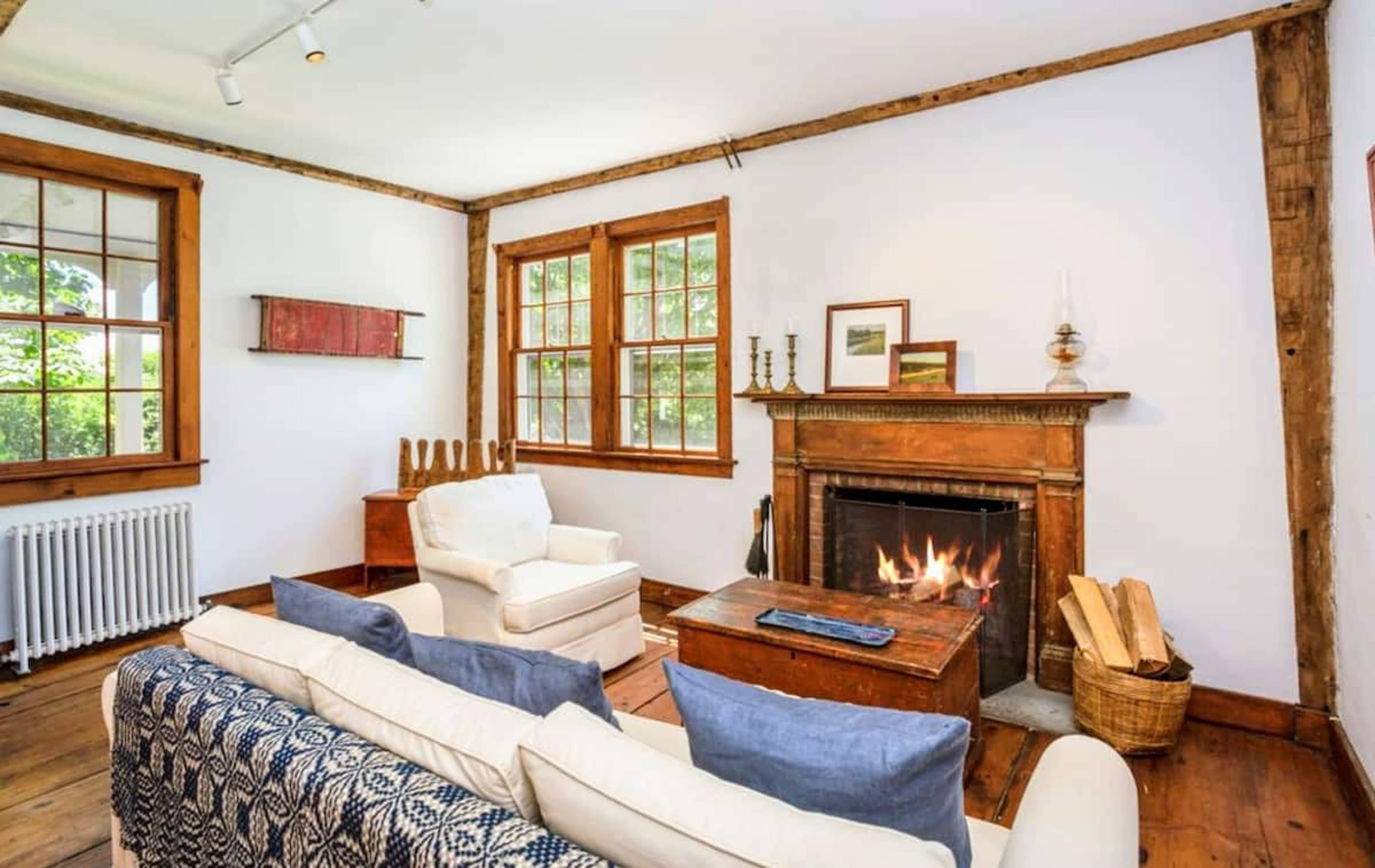 The image shows a cozy living room featuring a fireplace, wooden walls, and windows that allow natural light to enter the space.
