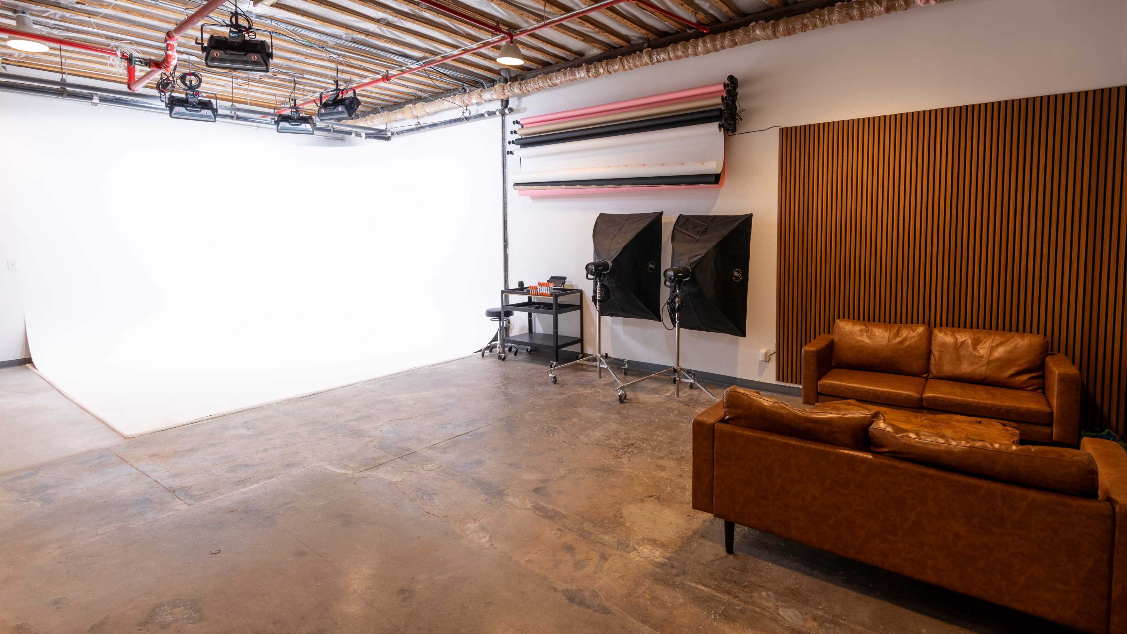 A photography studio featuring a white backdrop, studio lights, and a leather sofa against a wooden wall.