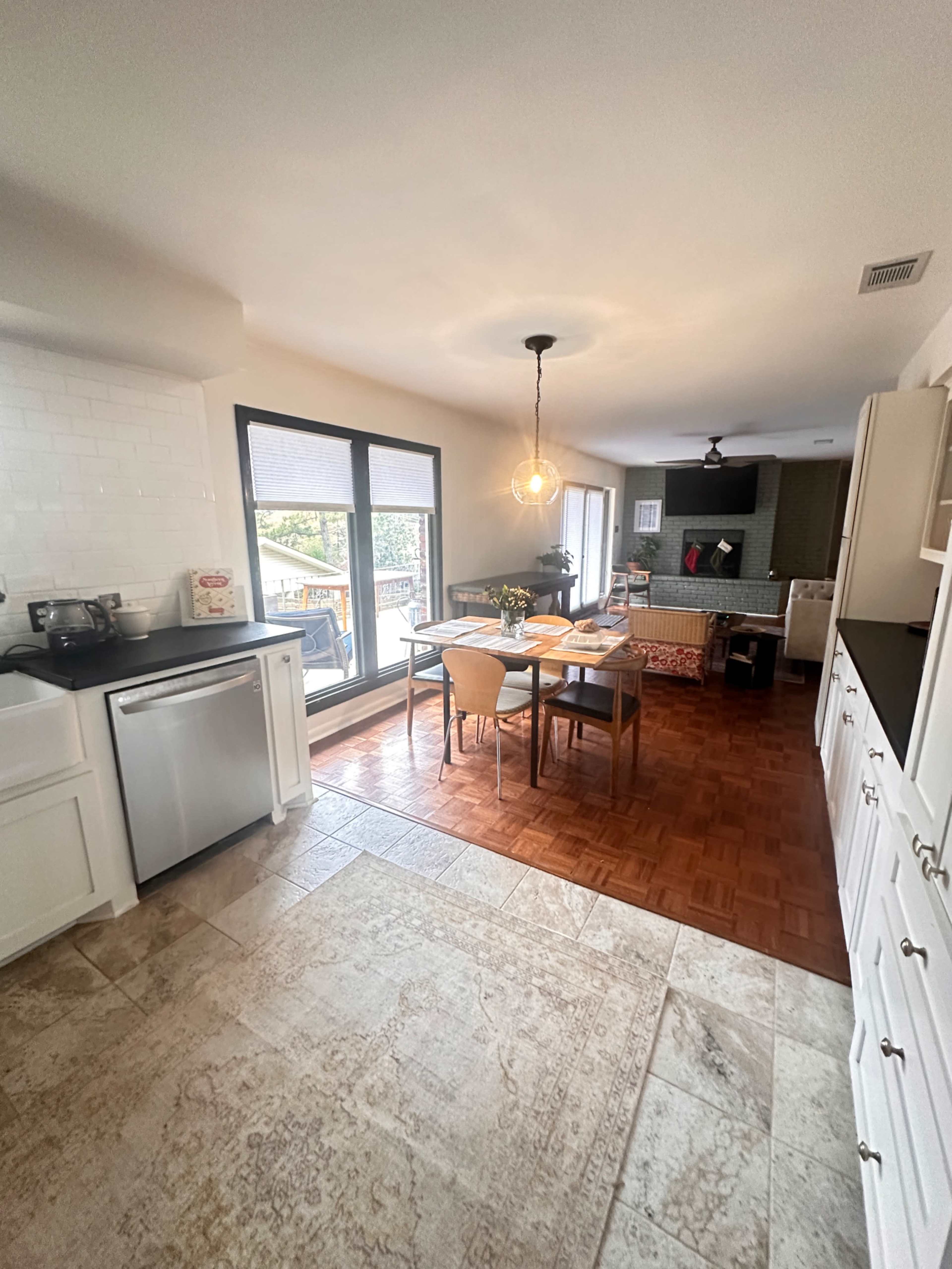 A modern kitchen features a dining area, large windows, and a mix of tile and wooden flooring.