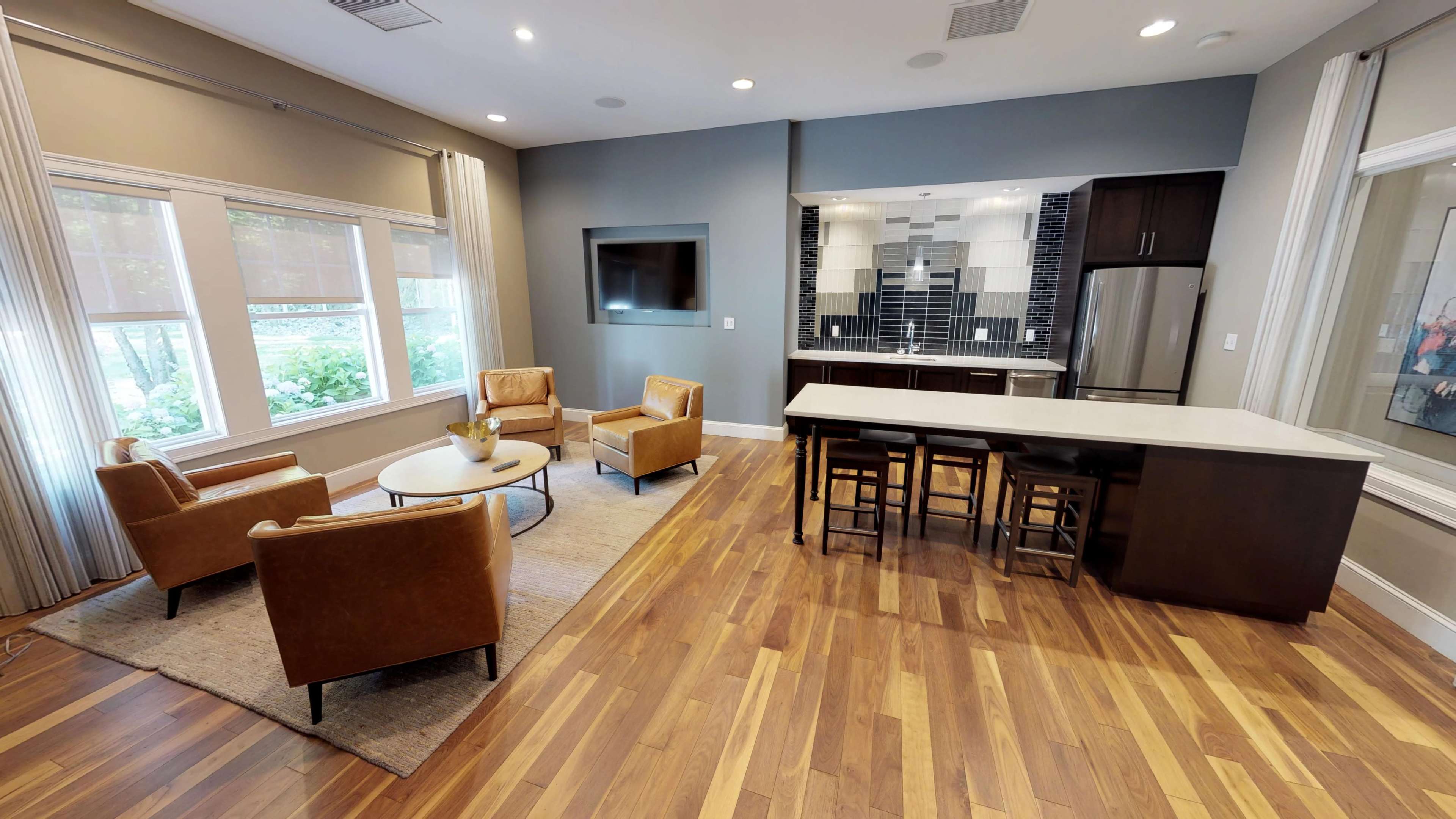 A modern living space with a seating area featuring two armchairs and a coffee table, alongside a kitchen with barstools and sleek appliances.