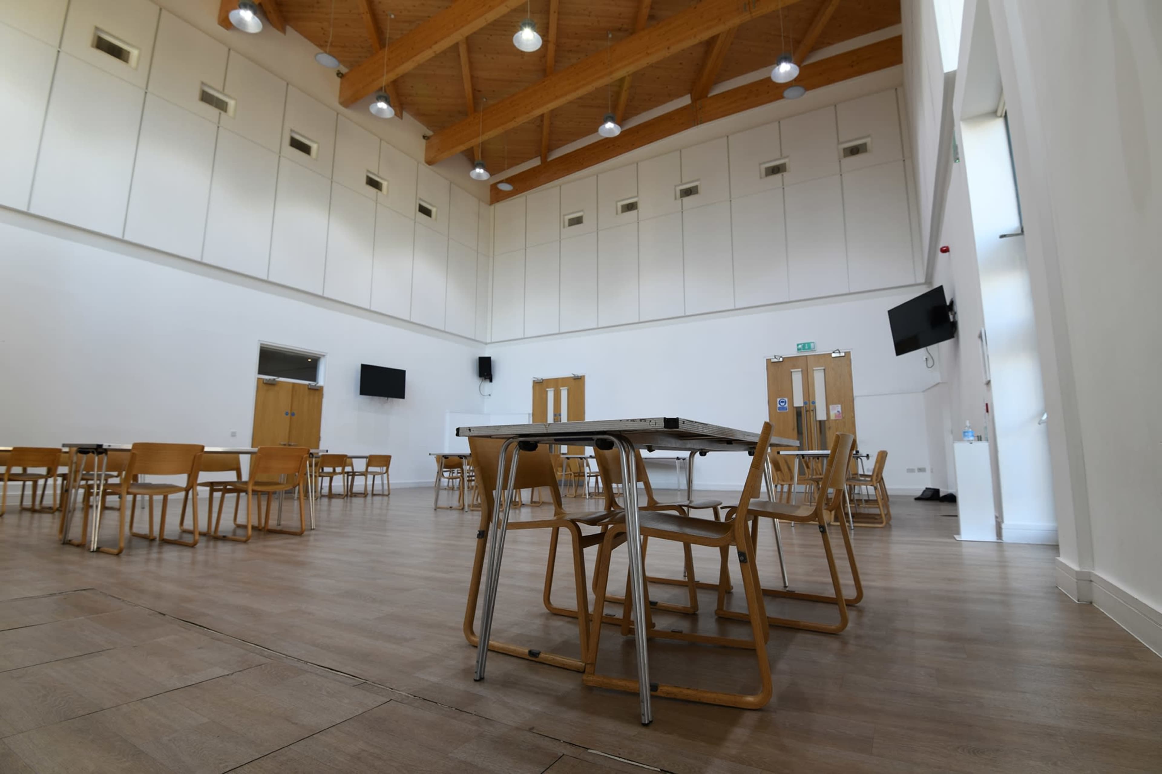 An empty indoor hall with wooden beams, several tables, and chairs arranged around the space.