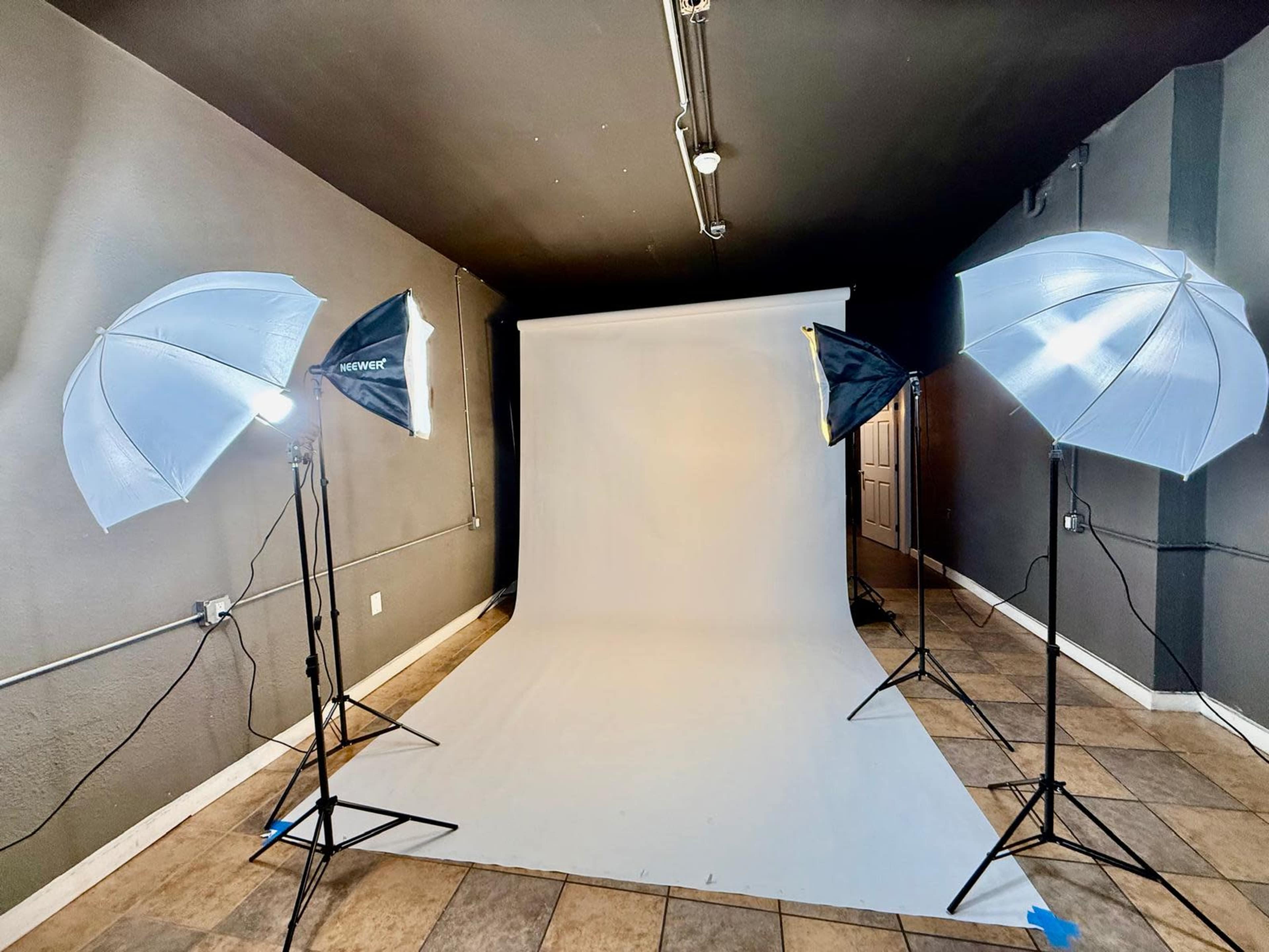The image shows a photography studio setup with four light umbrellas facing a plain white backdrop on the floor.