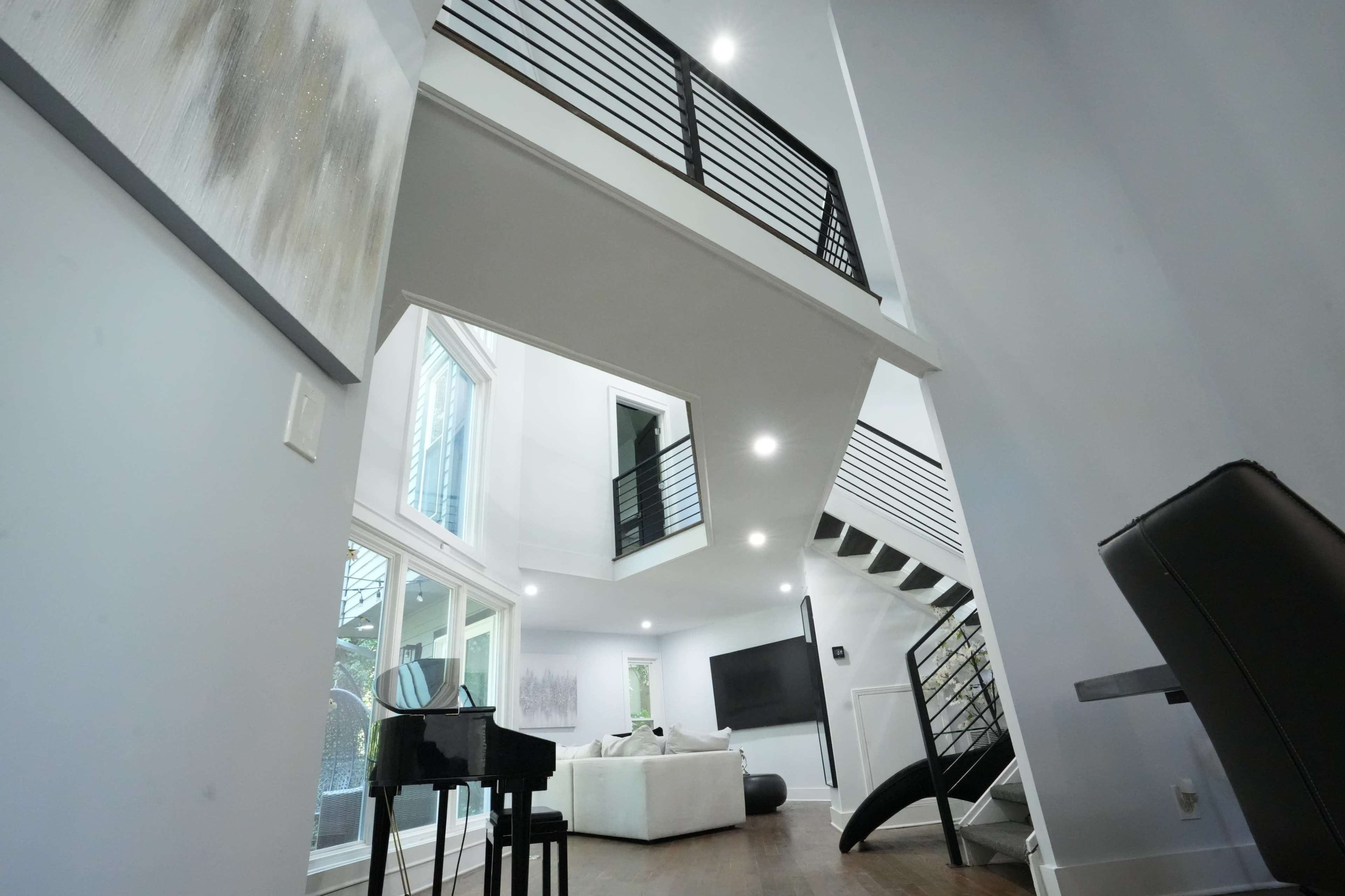 The image shows a modern interior space featuring an open layout with a staircase, large windows, and minimalist furniture.
