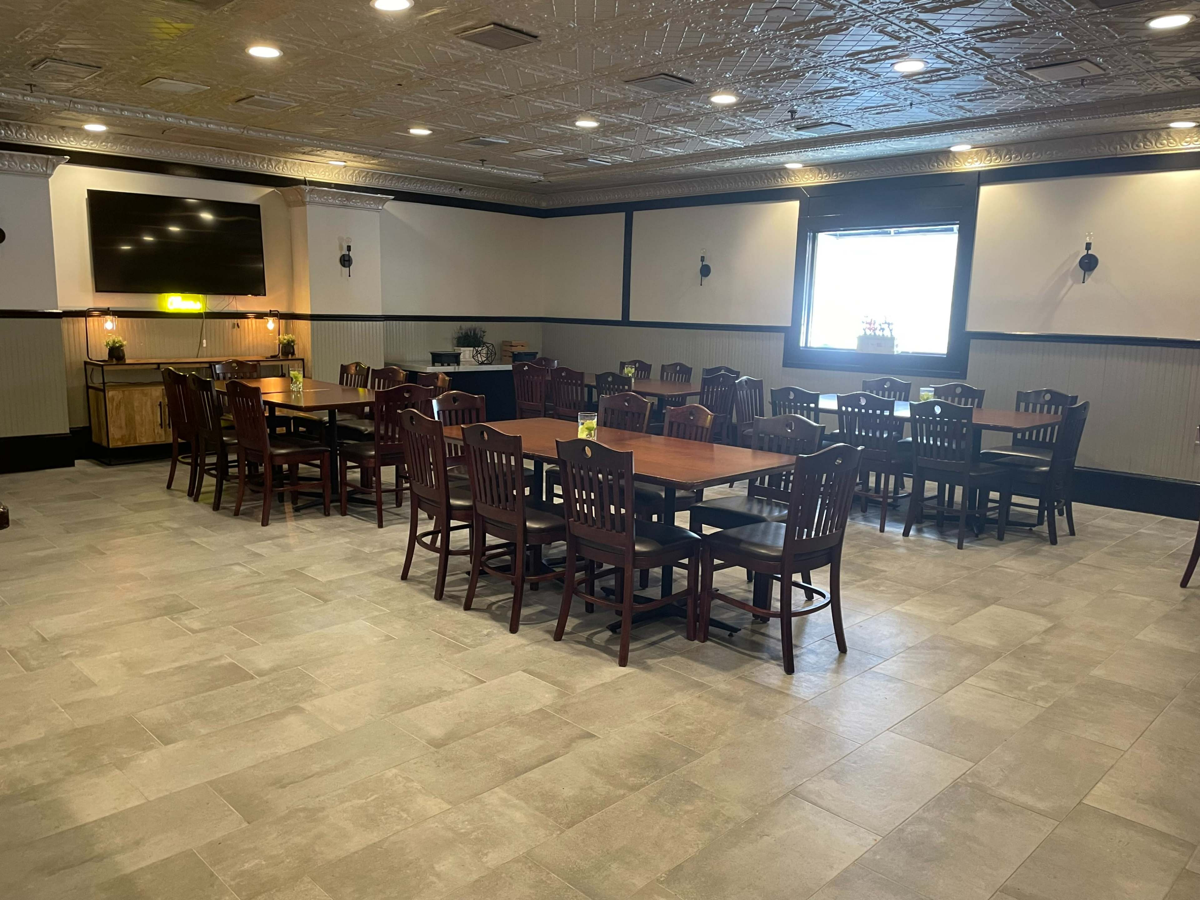 A spacious dining area features rows of wooden tables and chairs, with a large TV mounted on the wall.