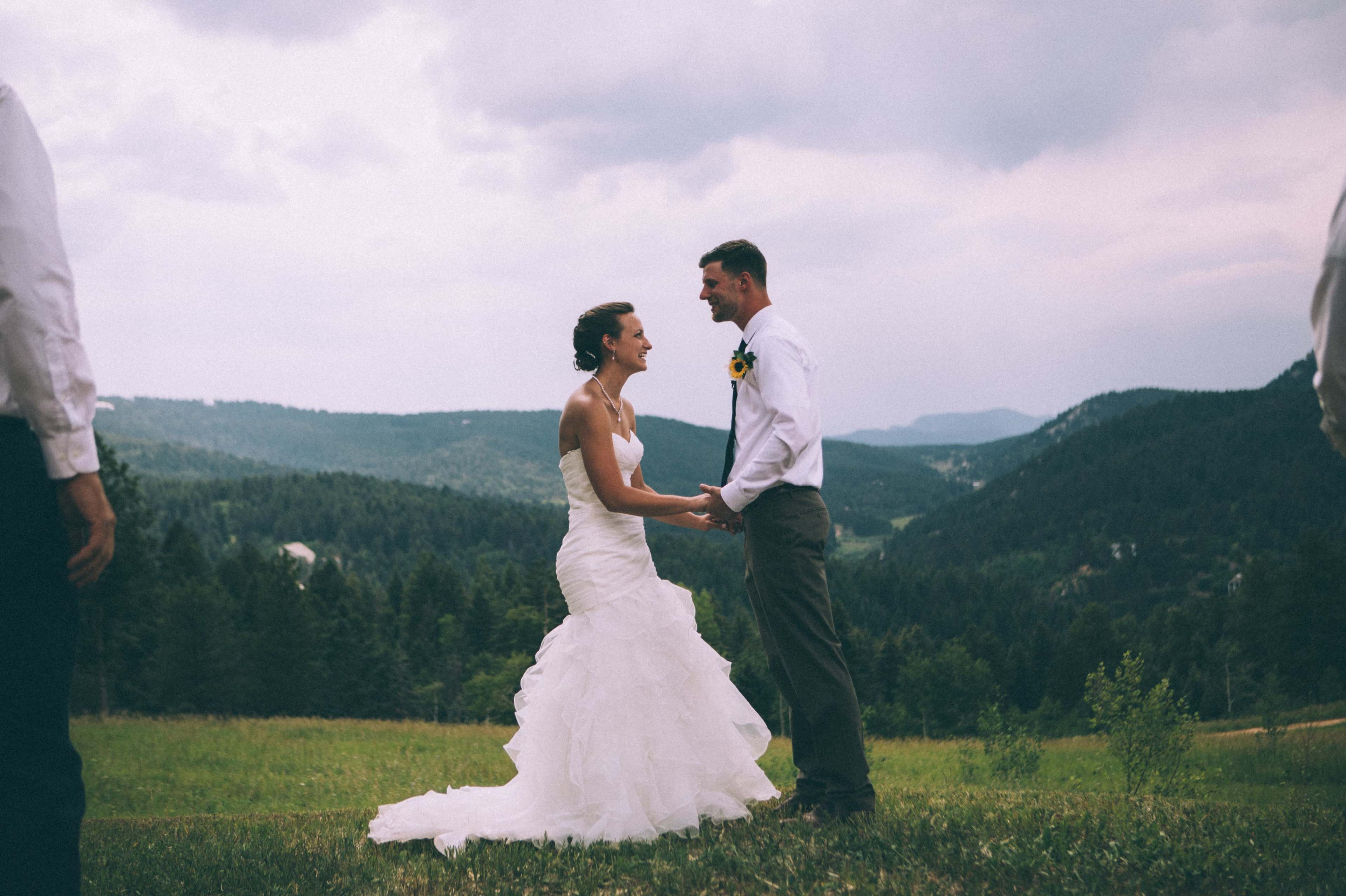 A bride and groom hold hands during their outdoor wedding ceremony in a mountainous landscape.