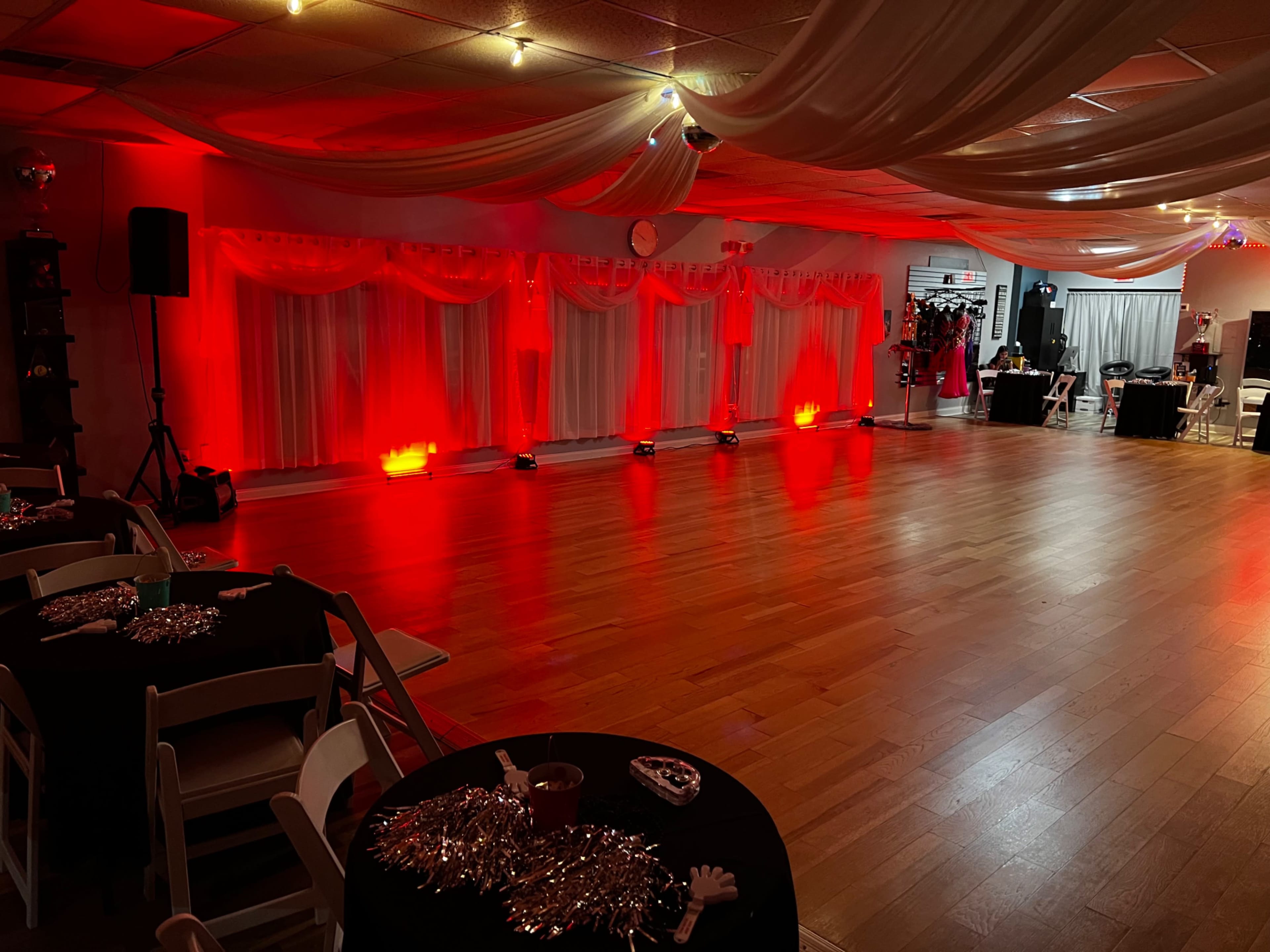 A spacious event hall decorated with red lighting, draped fabric, and black table settings for a gathering.