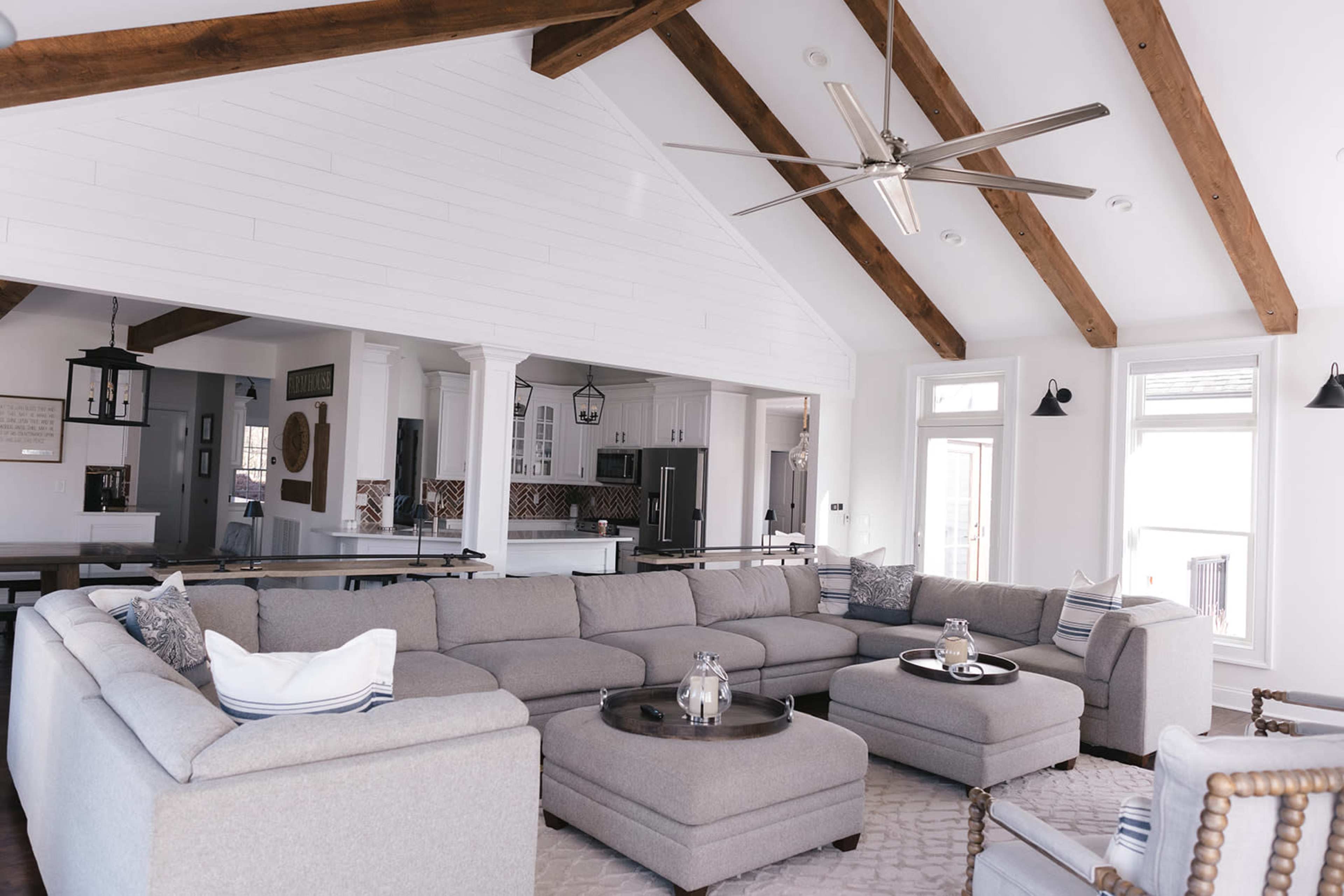 A spacious living room features a large gray sectional sofa, a circular coffee table, and exposed wooden beams in the ceiling.