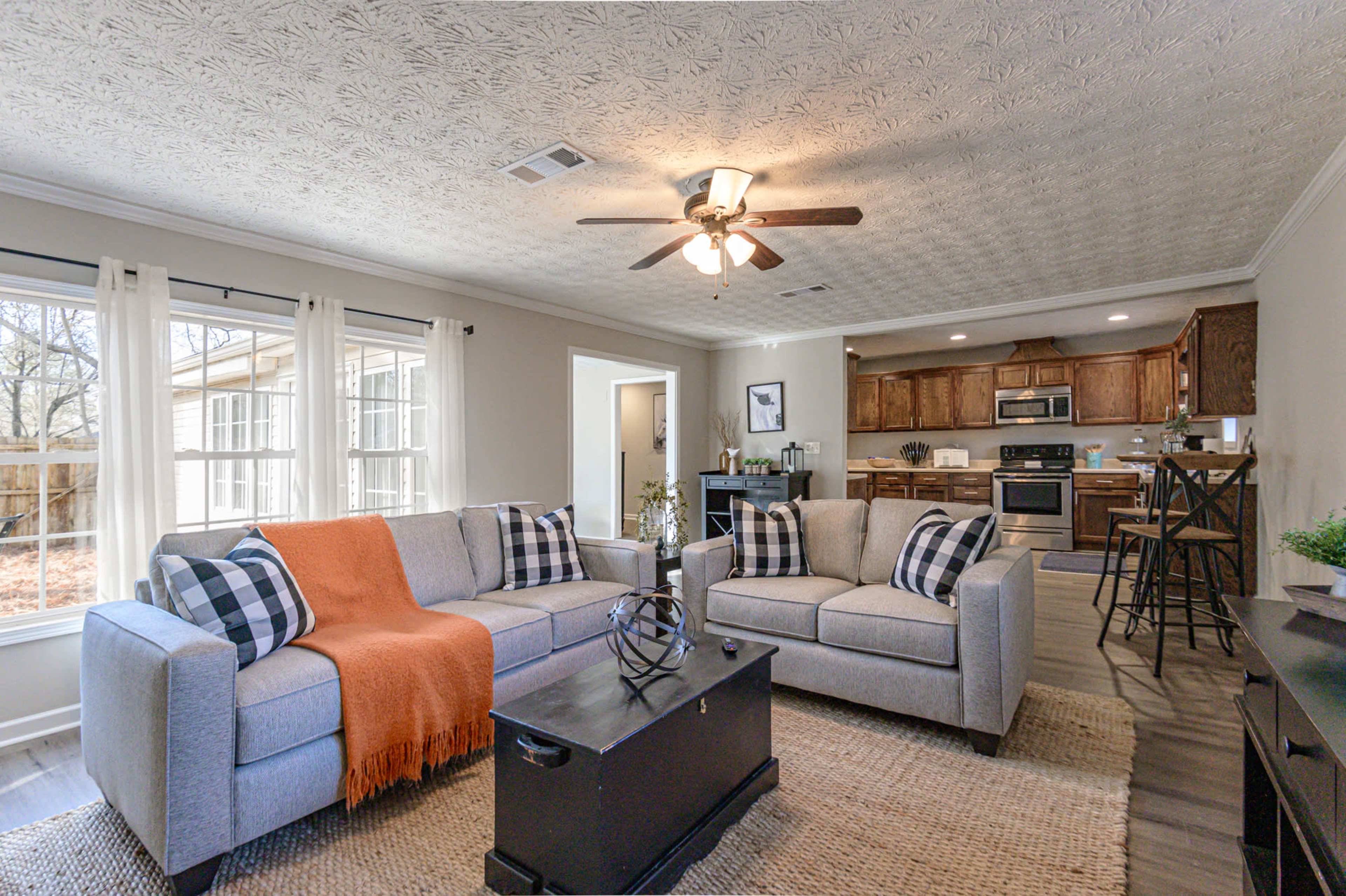 A neatly arranged living room with two gray sofas, a coffee table, and a view of a kitchen in the background.