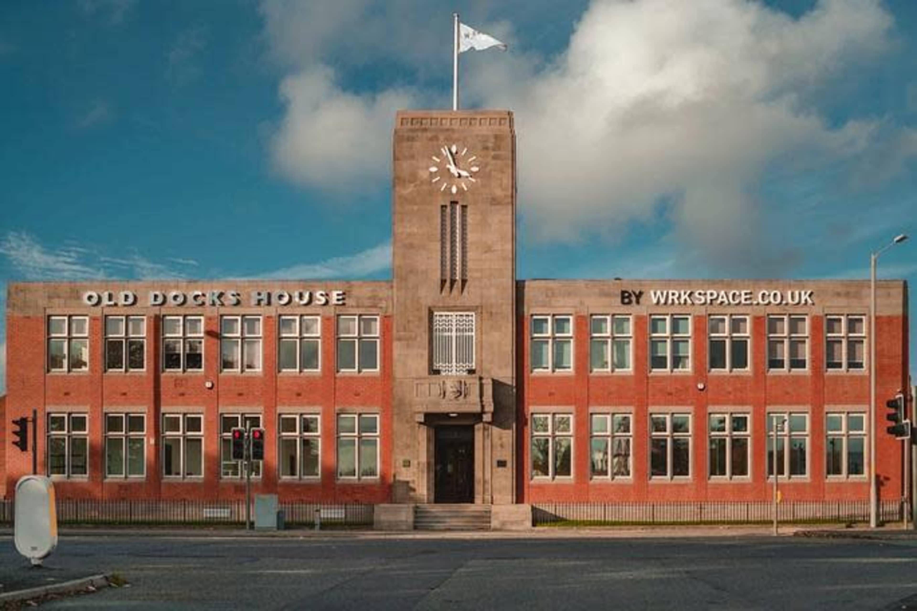 The image shows a brick building with a clock tower and large windows, labeled "Old Docks House" in bold letters, located at a street intersection.