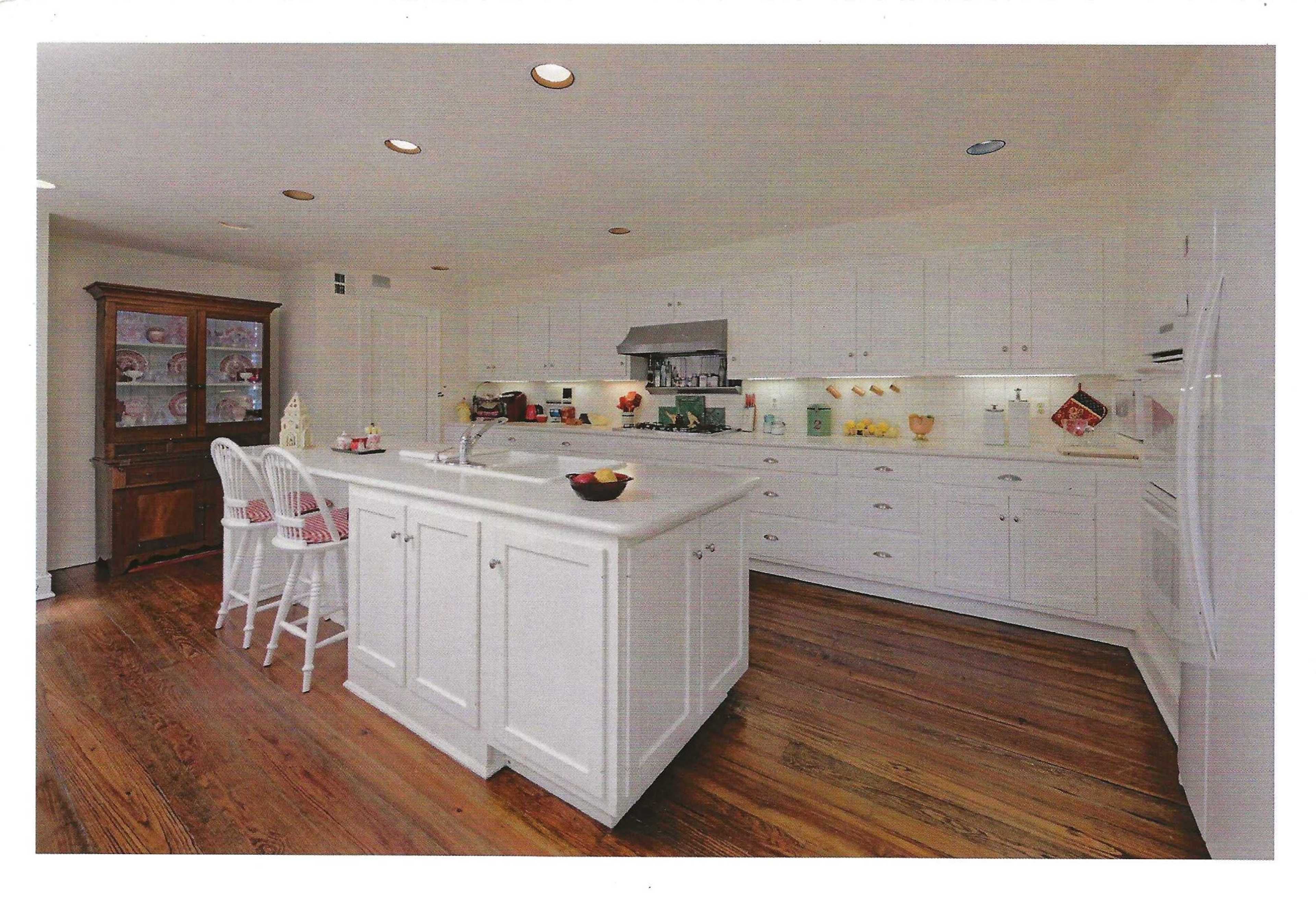 The image depicts a spacious kitchen with white cabinetry, a large island, and wood flooring.