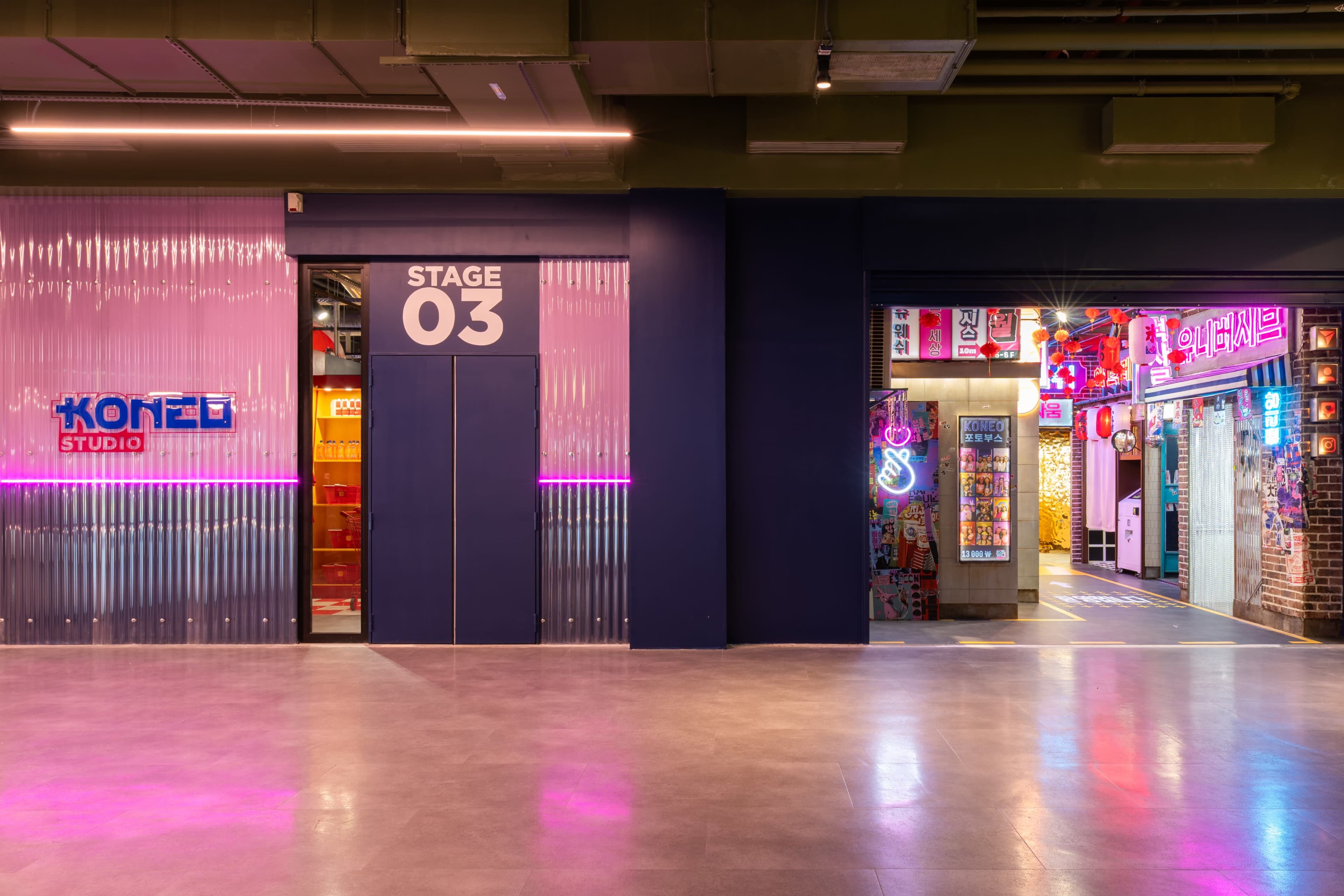 The image shows two adjacent entrances in a modern venue, one labeled "KOREA STUDIO" and the other labeled "STAGE 03," with colorful neon lights and vibrant decorations visible through the open door.