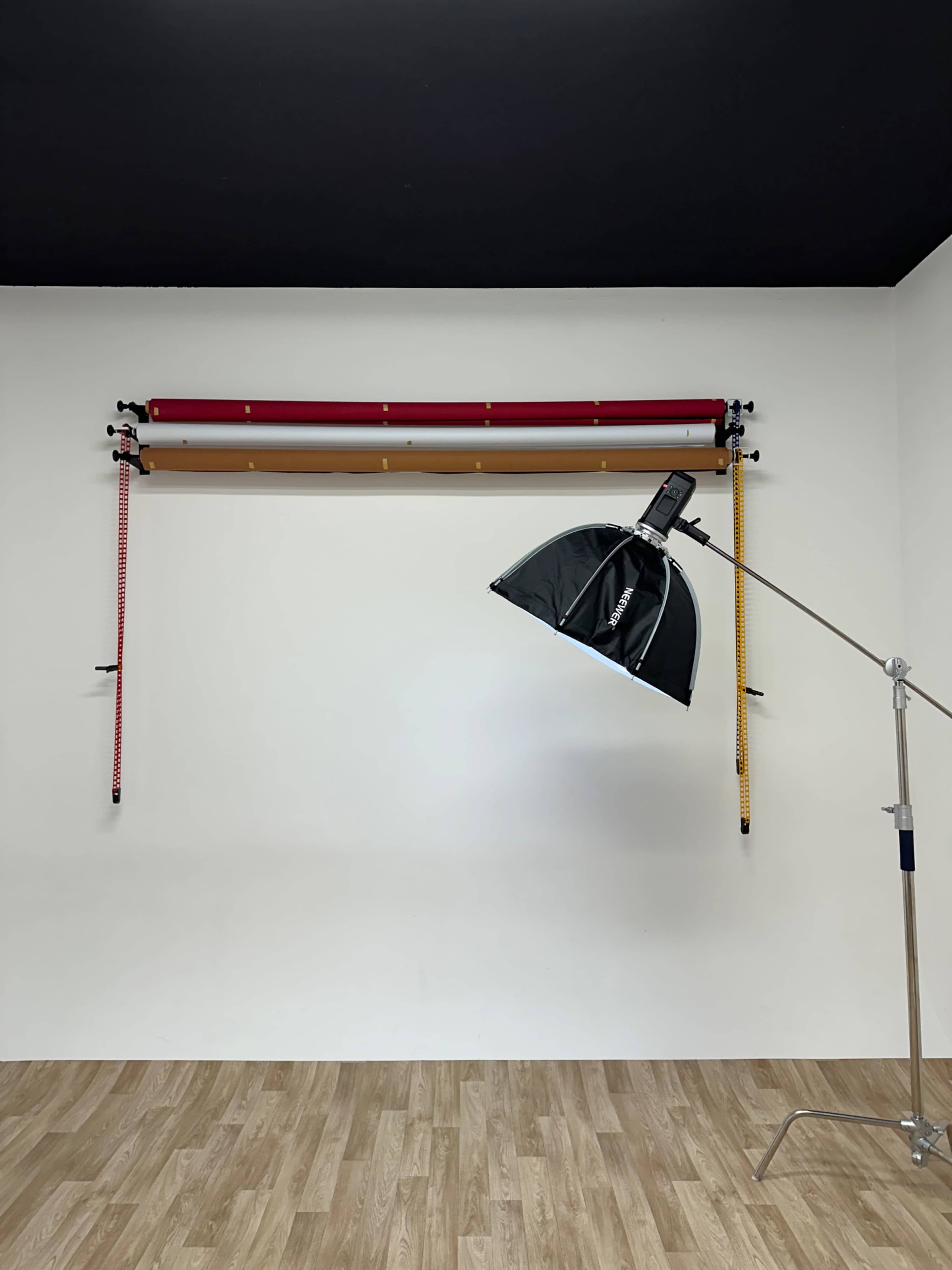 The image shows a studio setup with a backdrop hanging on the wall and a light stand with an umbrella-style softbox in front of it.
