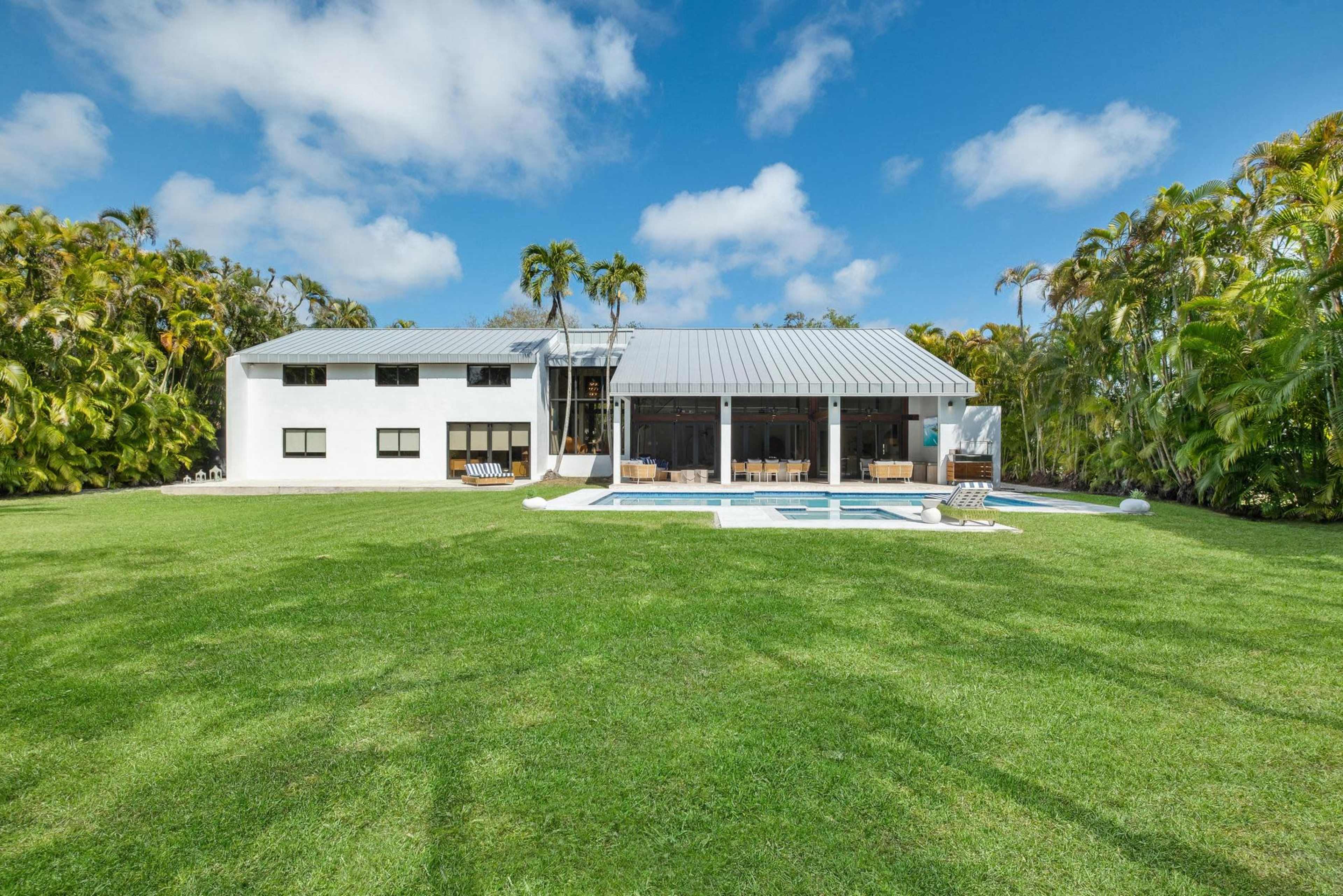 A contemporary two-story house with a metal roof and large windows sits next to a swimming pool, surrounded by lush greenery.