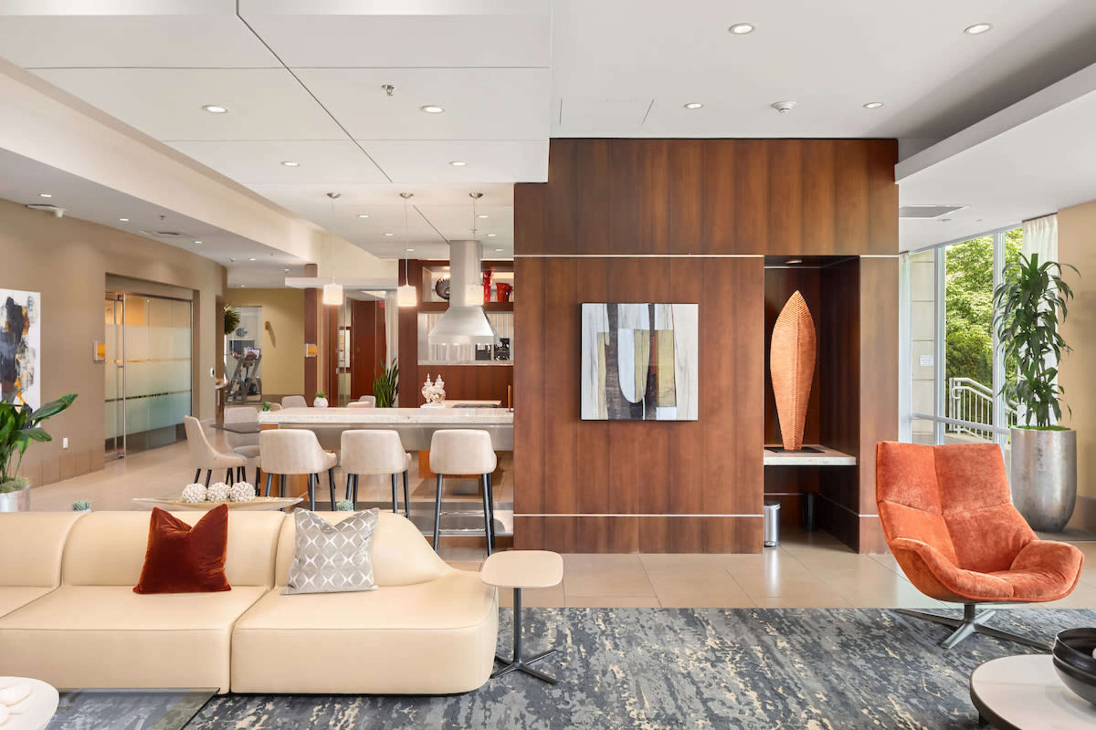 A modern lobby area featuring a light-colored sofa, an orange armchair, a bar-style seating area, and decorative artwork on the walls.