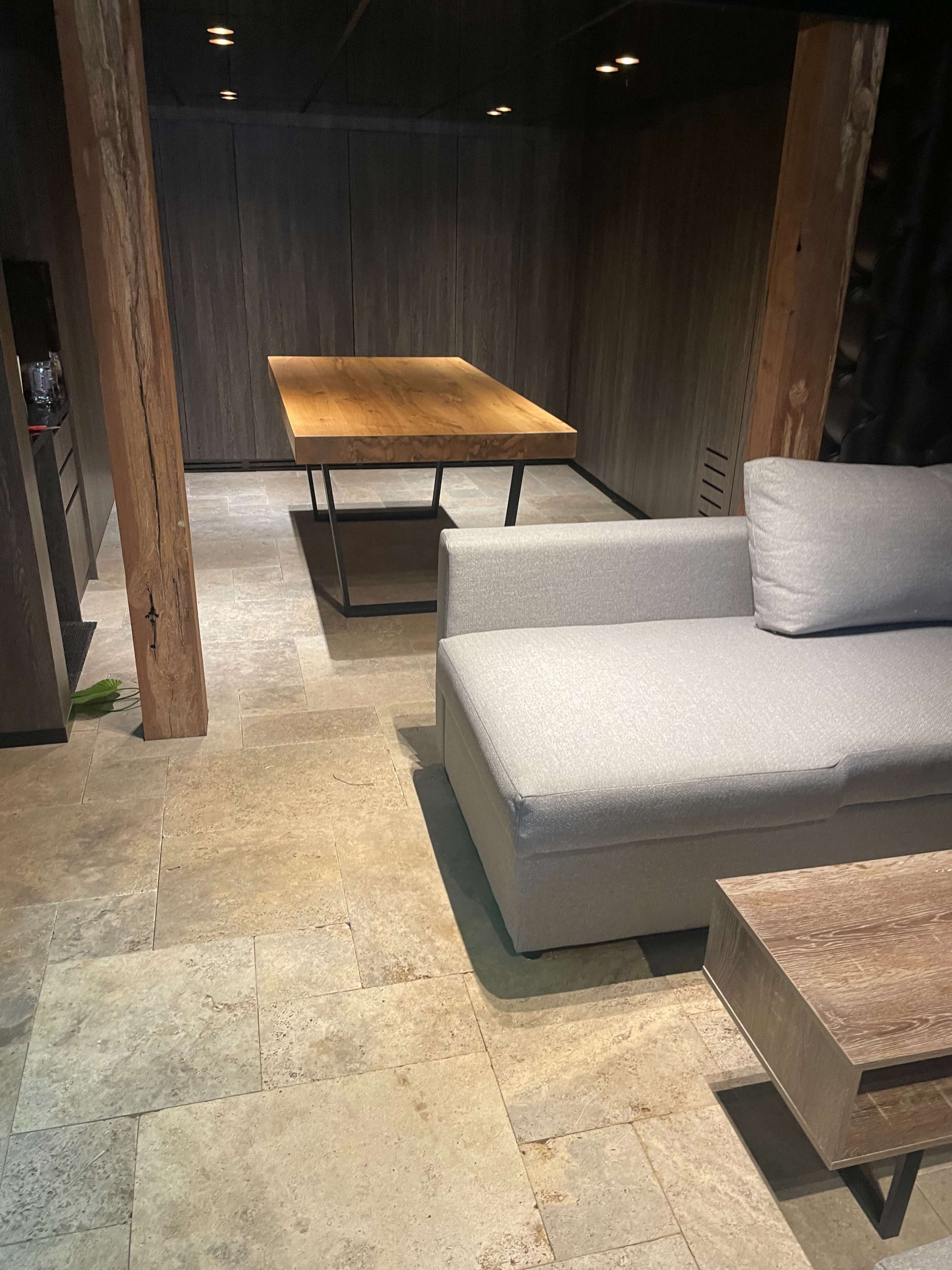 A modern interior space featuring a gray sofa, a wooden dining table, and stone tiled flooring.