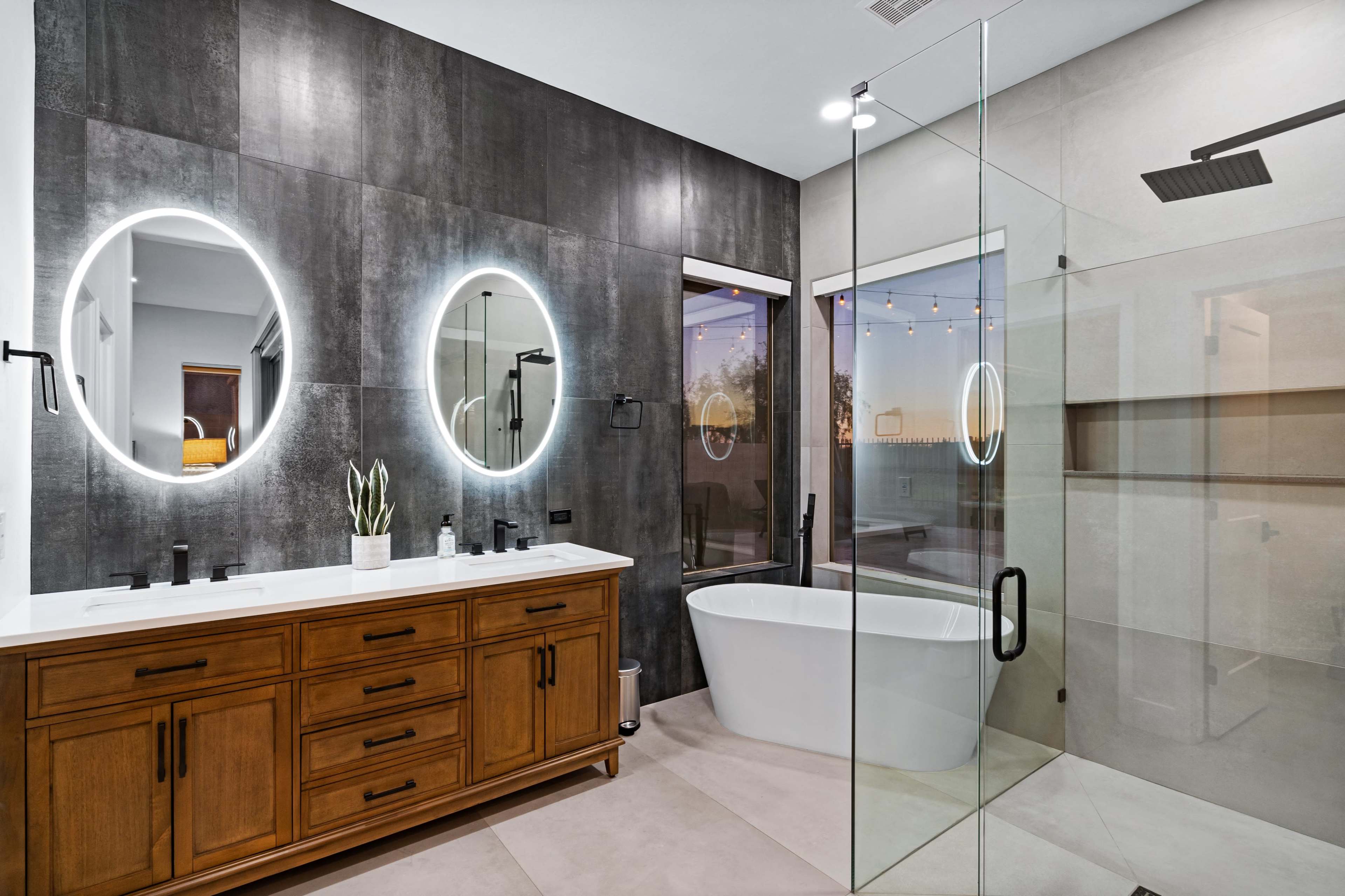 A modern bathroom featuring a double vanity with circular mirrors, a freestanding bathtub, and a glass shower enclosure.