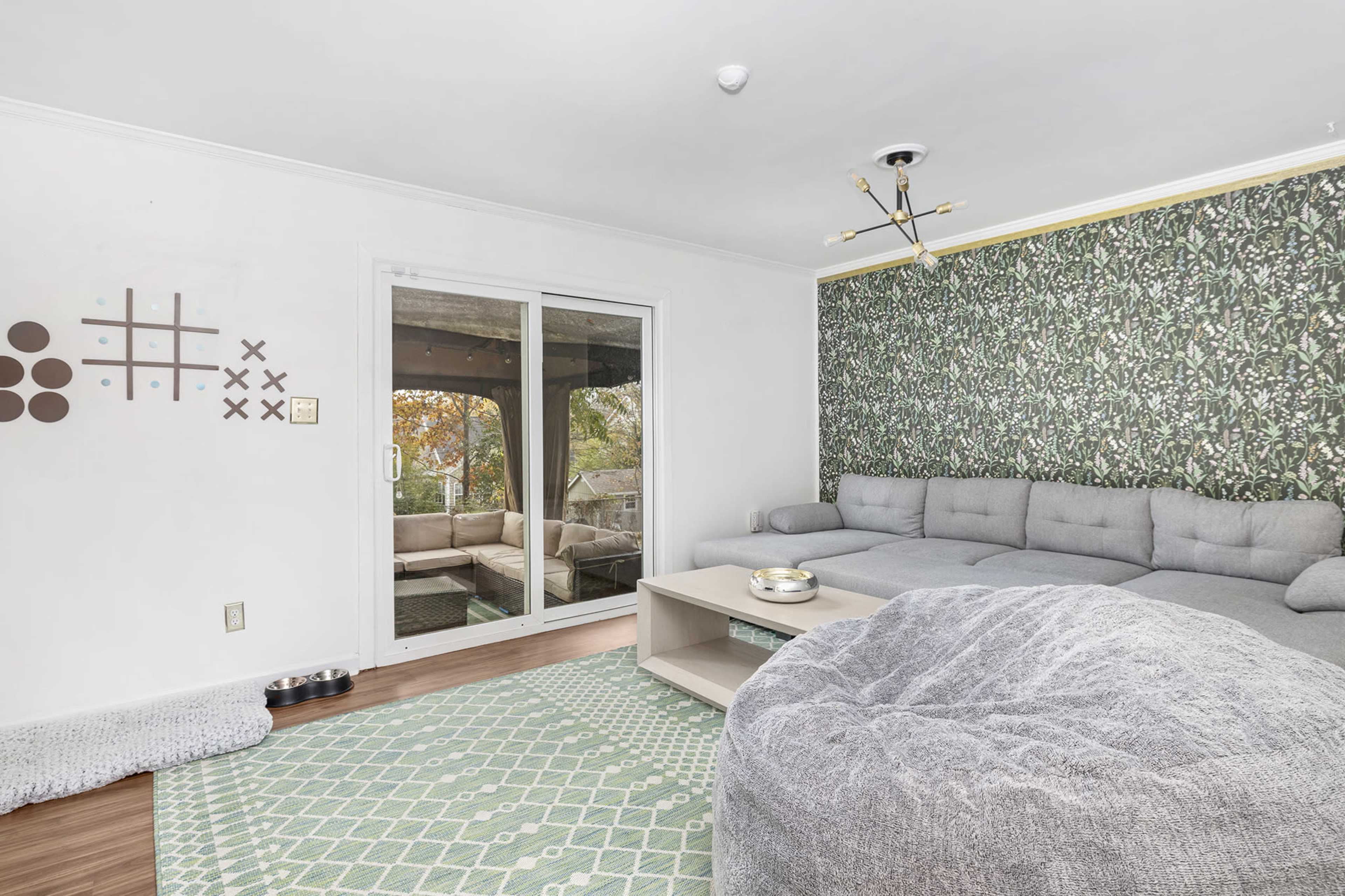 The living room features a large sectional sofa, a round coffee table, and a sliding glass door overlooking a patio area.