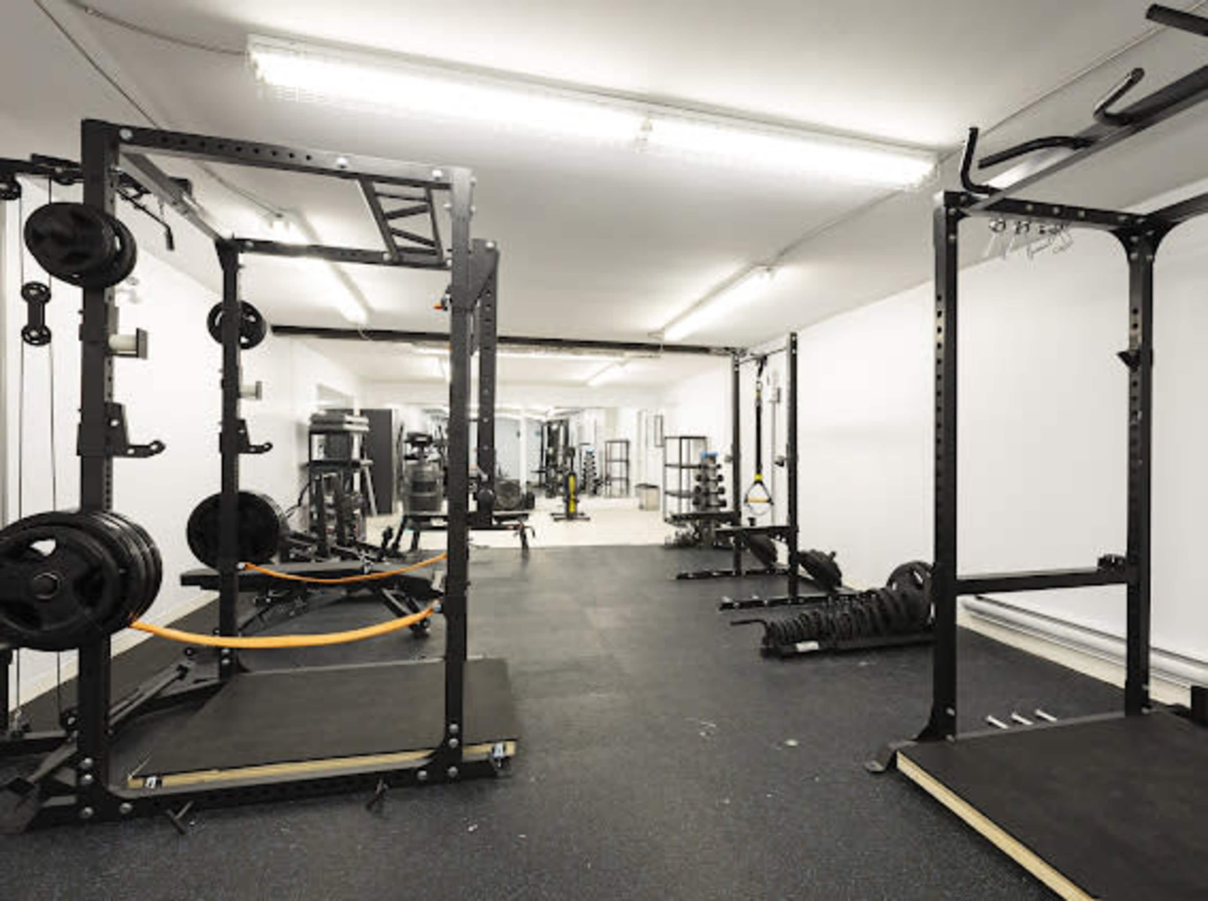 A spacious gym featuring various weightlifting equipment, including squat racks, barbells, and resistance bands on a black rubber floor.