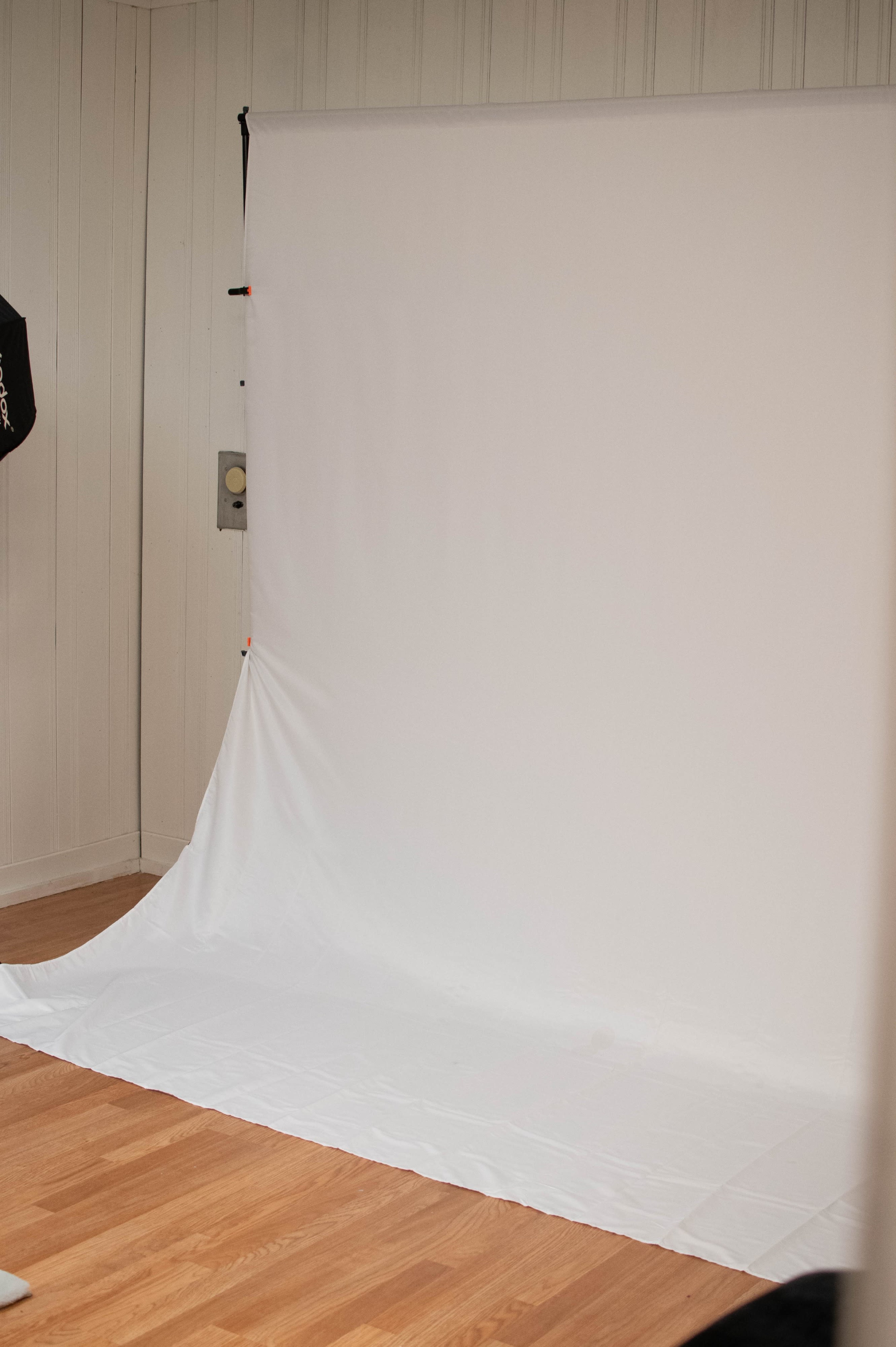 A white backdrop is set up on a hardwood floor in a brightly lit room.