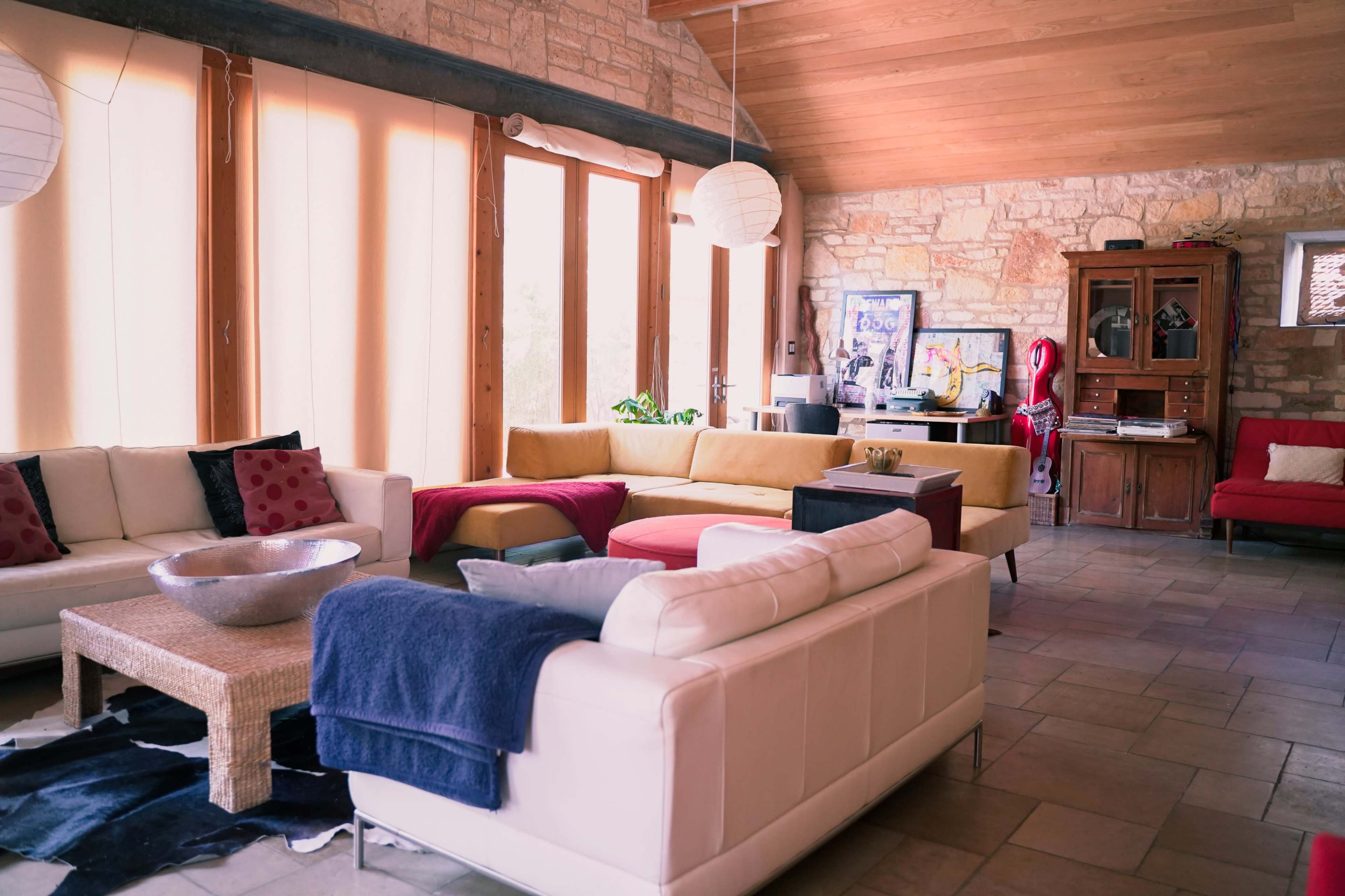 The living room features various seating arrangements with a mix of colors, large windows letting in natural light, and stone walls.