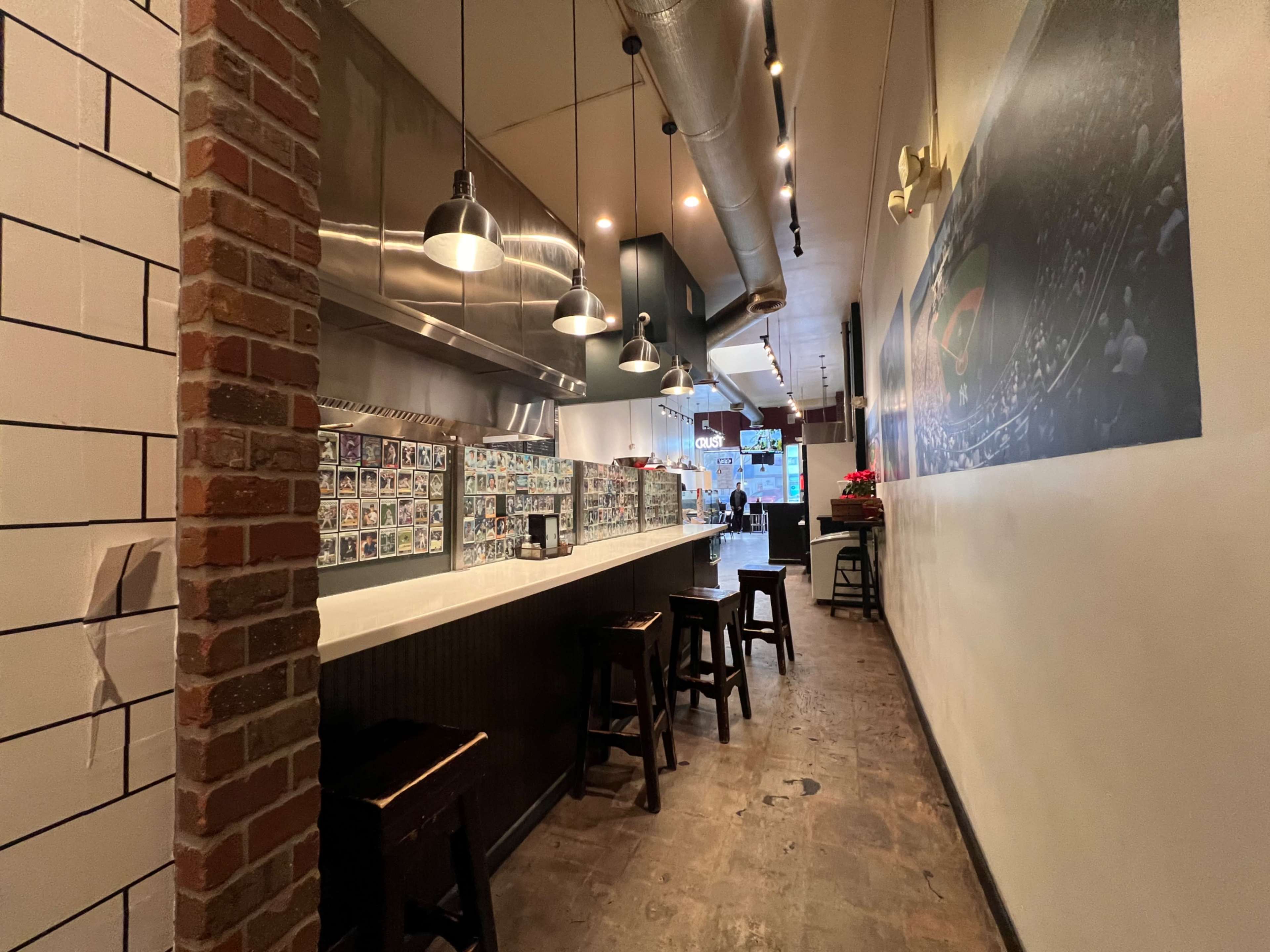 The image shows a narrow restaurant interior with a bar counter, metal lighting fixtures, and a wall adorned with framed photographs.