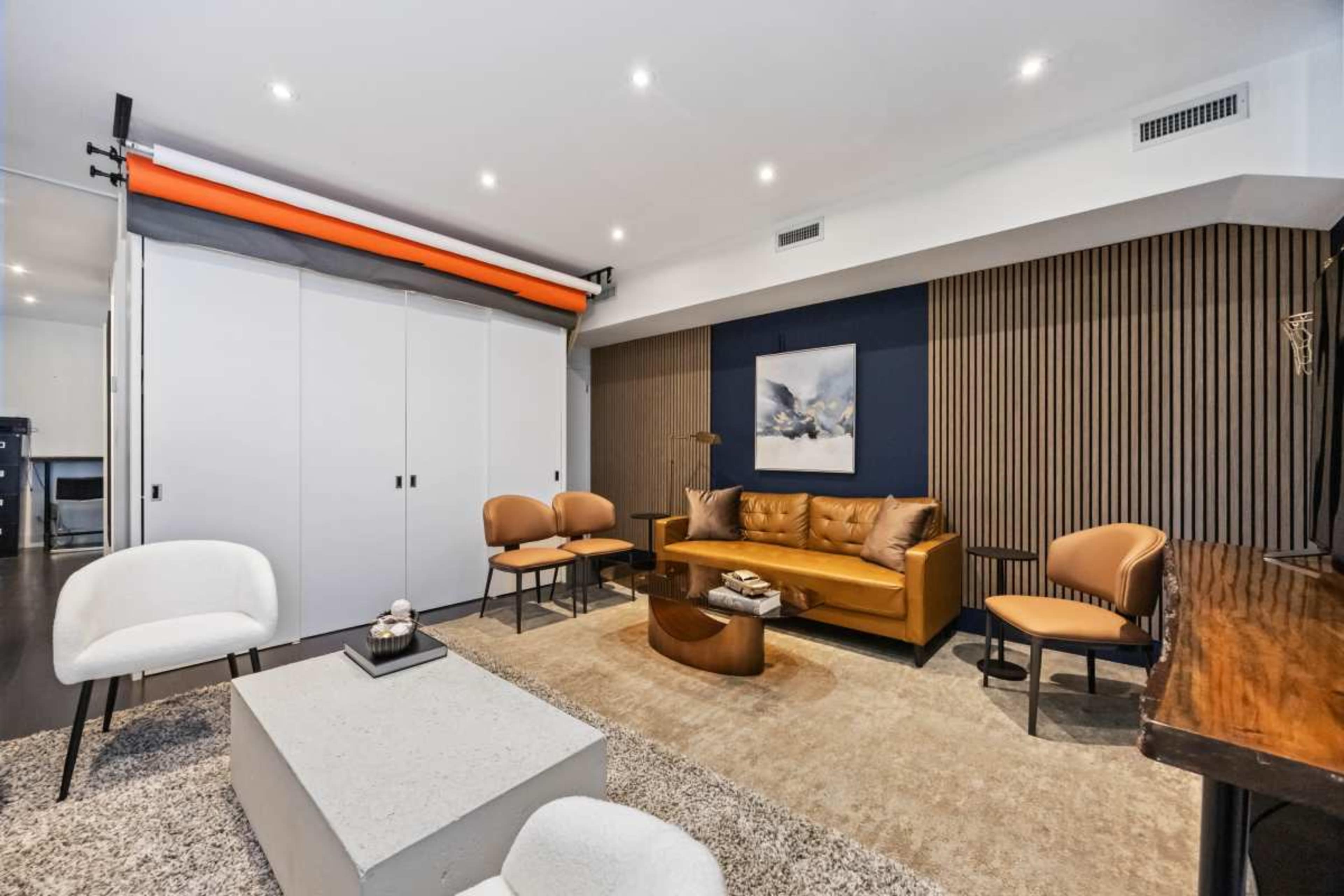 The image shows a modern living room with a brown leather sofa, three chairs, a coffee table, and a large area rug, all arranged around a minimalist design.