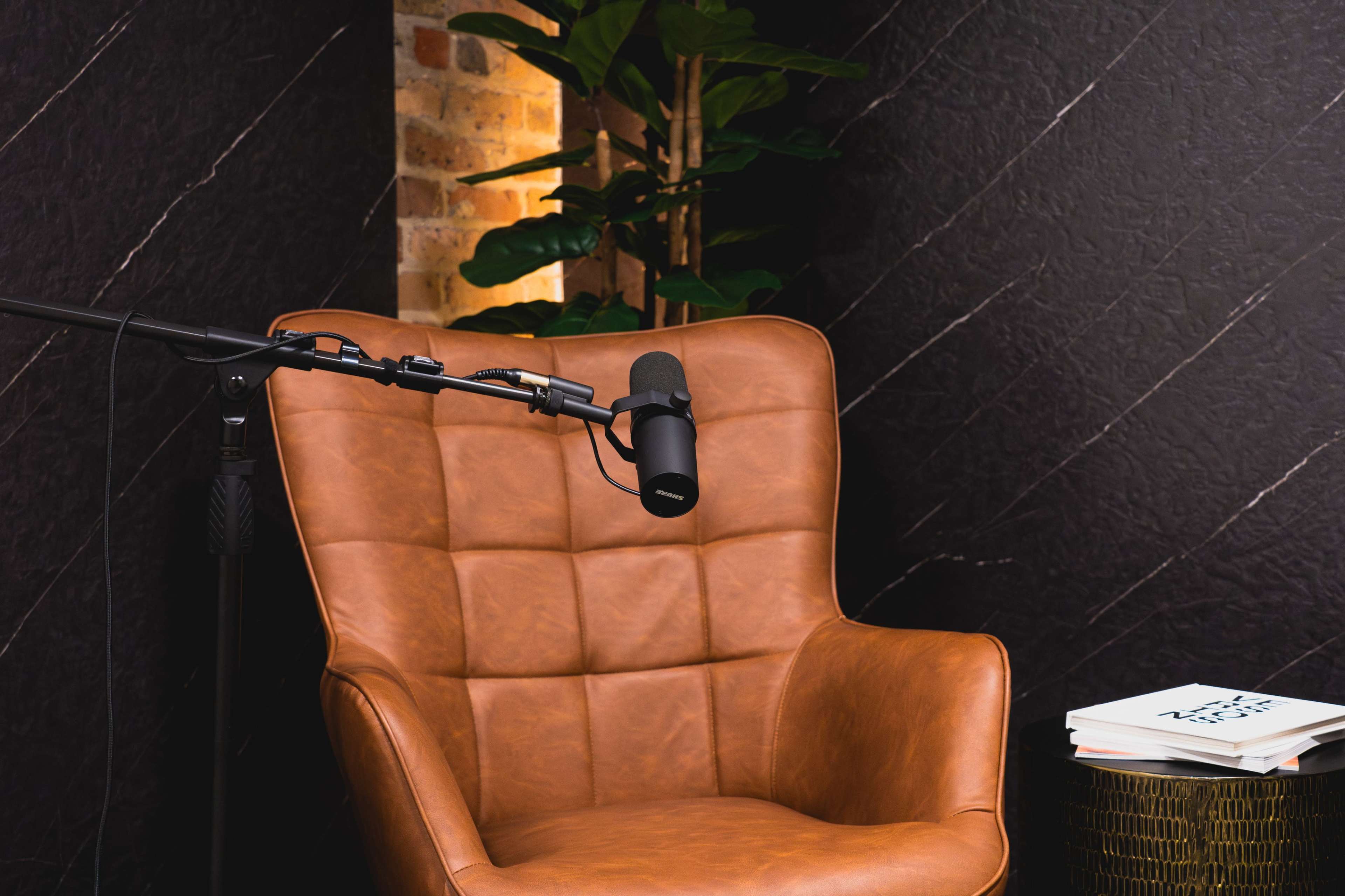 The image shows a brown leather armchair next to a side table with stacked books and a microphone on a stand positioned nearby.