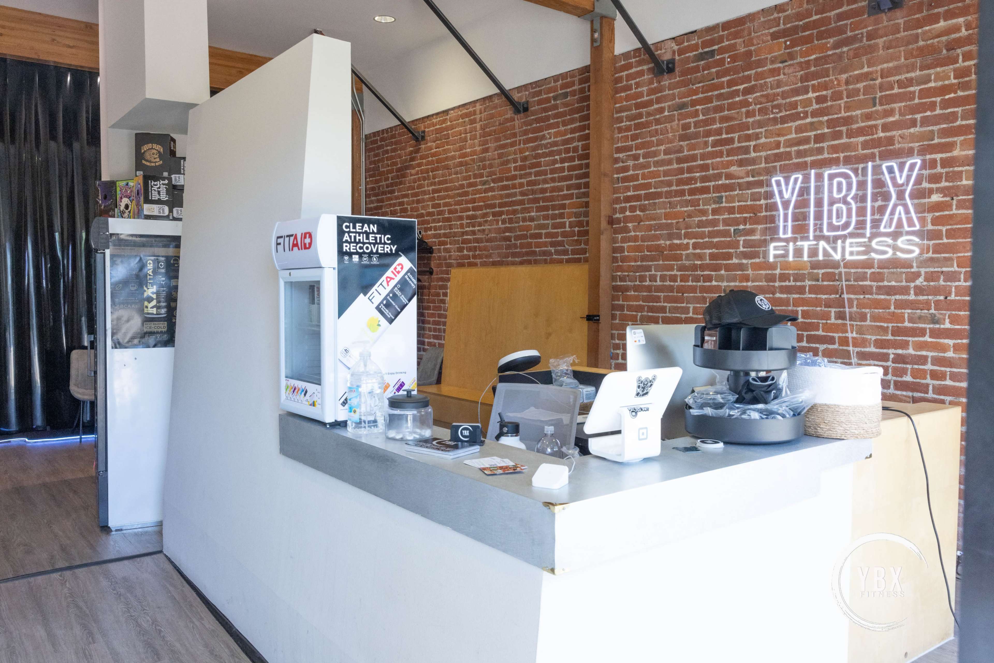 A fitness studio reception area with a brick wall, a counter equipped with a cash register, and promotional materials on display.