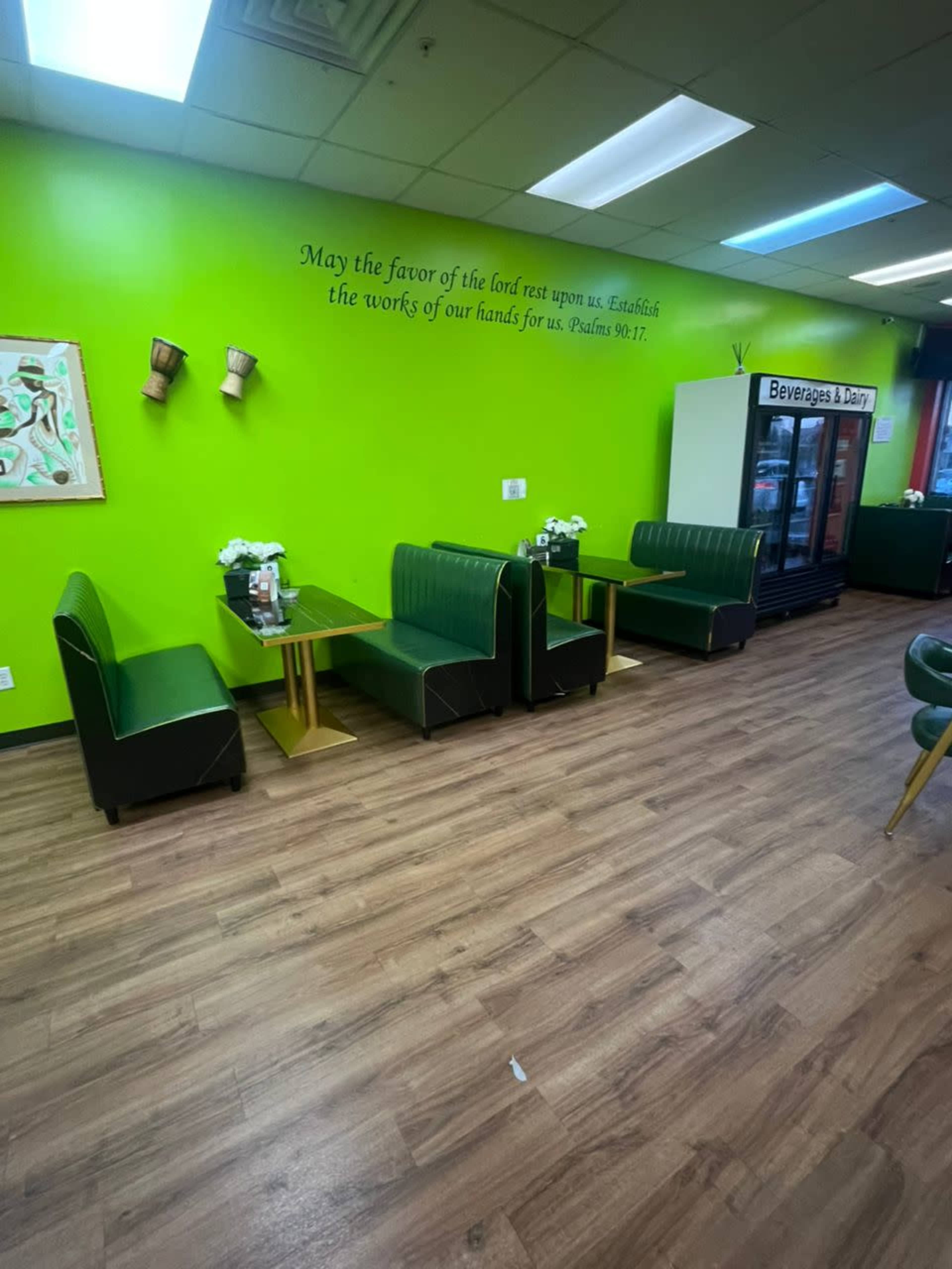 The image shows a brightly colored green cafe interior with green booths and a beverage fridge in the background.