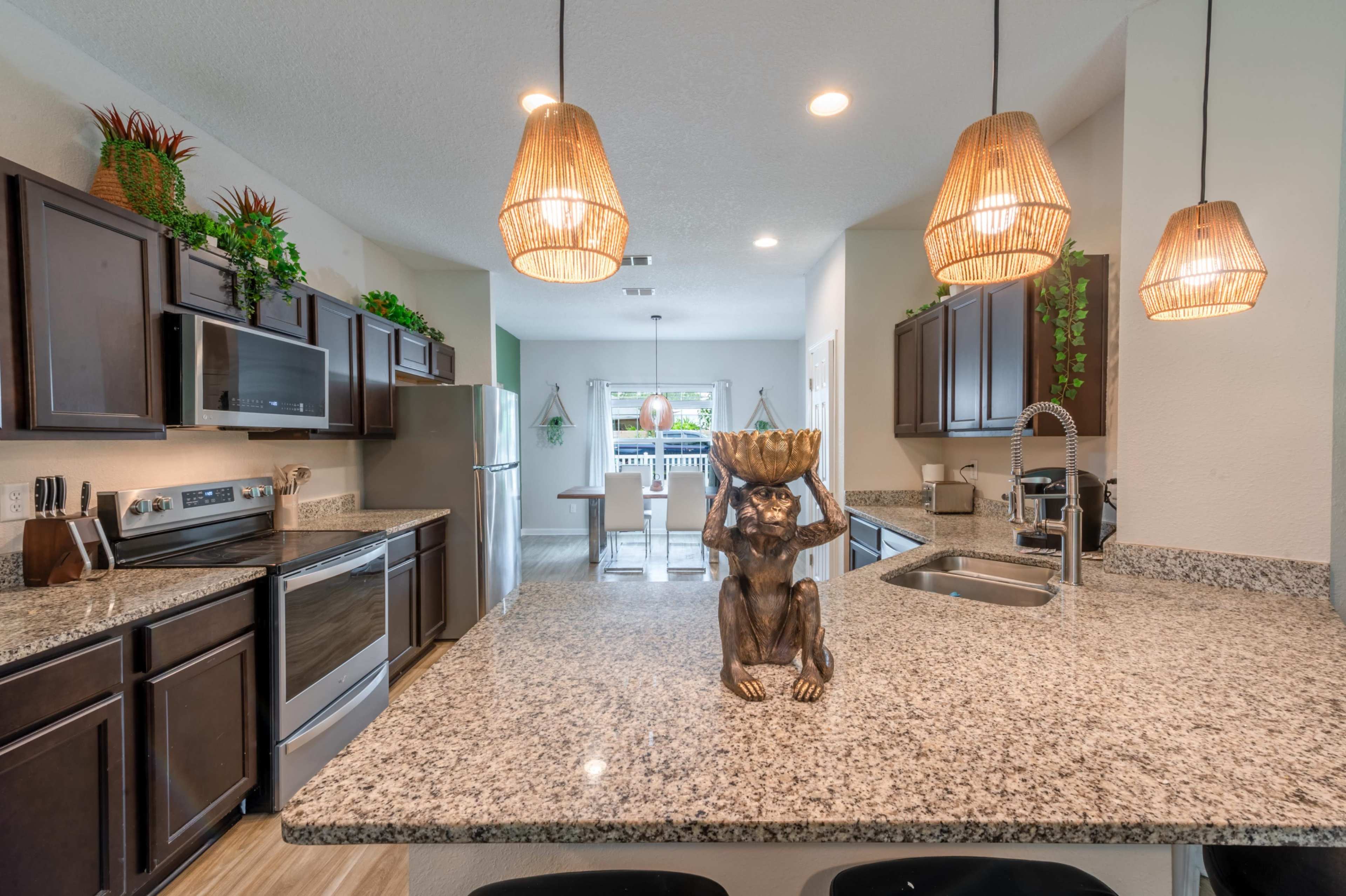 A modern kitchen features dark wood cabinets, stainless steel appliances, and a large granite island with decorative items and pendant lighting.