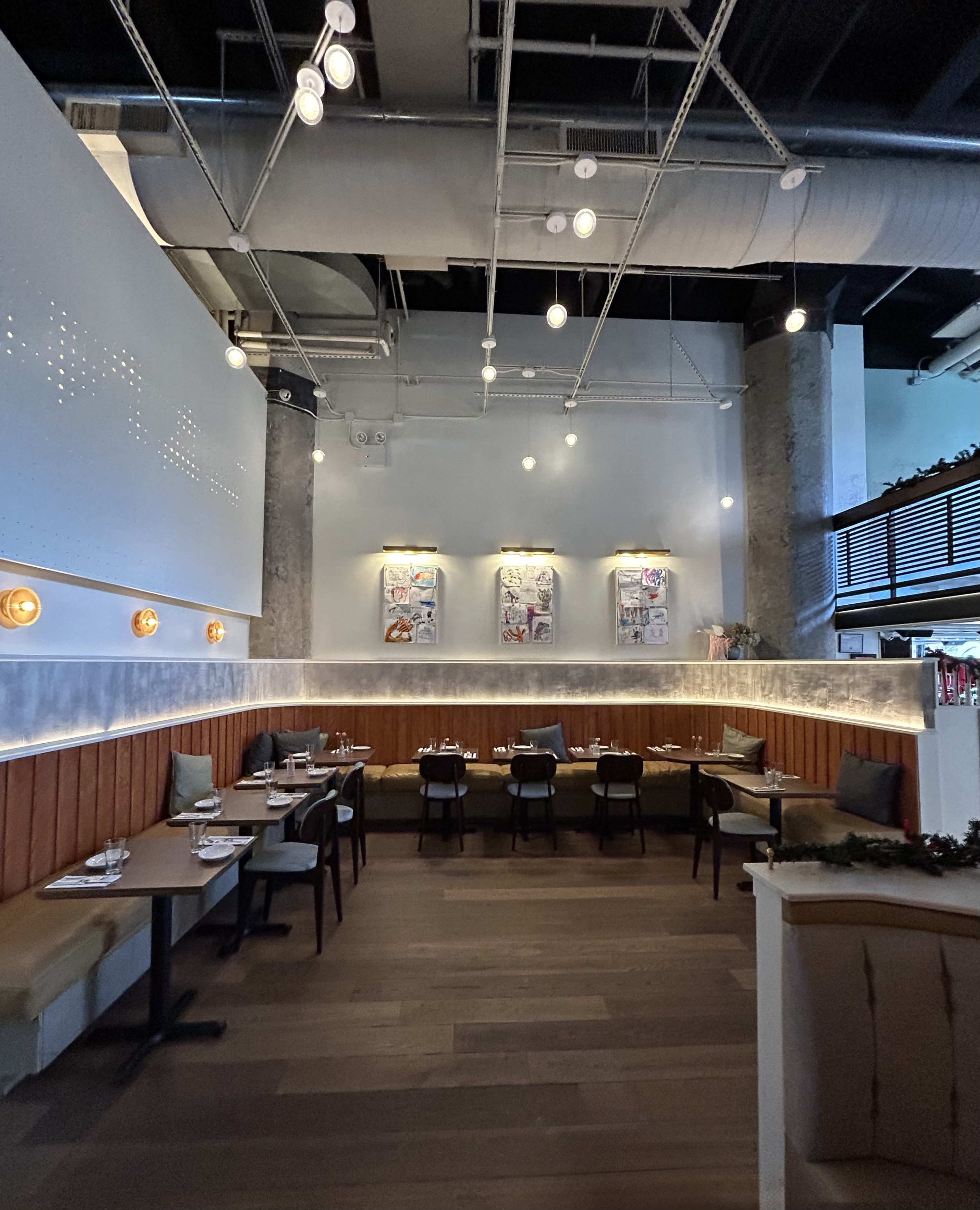 The image shows a modern restaurant interior with wooden paneling, a series of framed artworks on the wall, and tables set for dining.