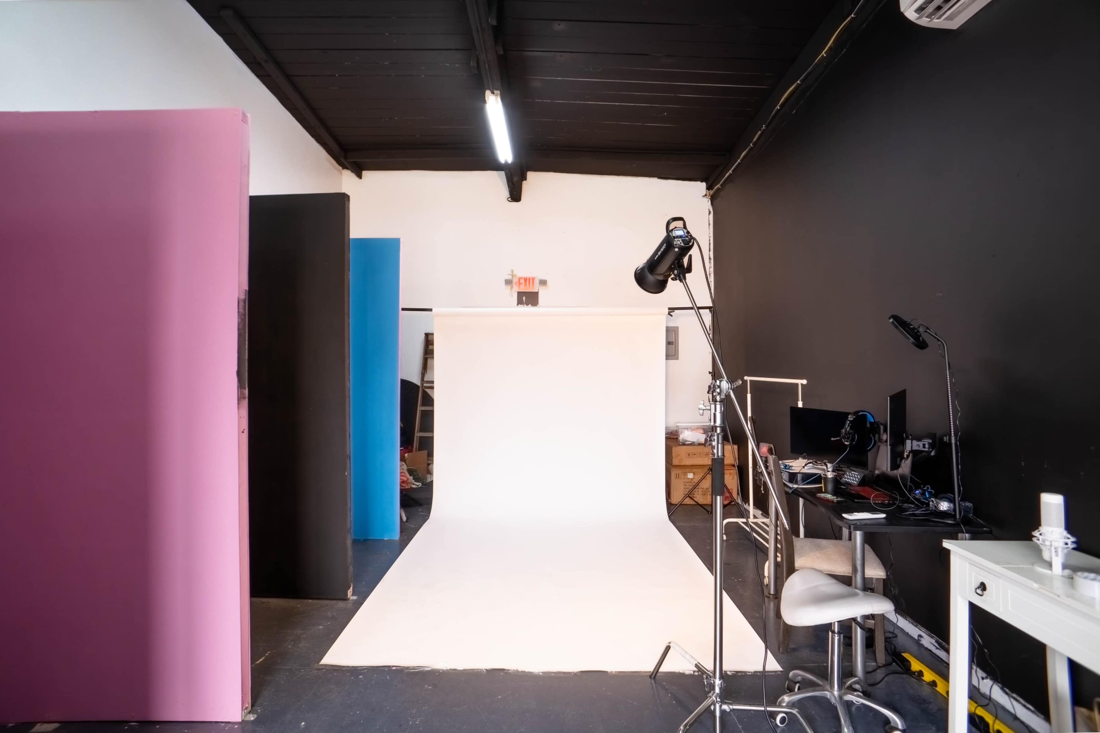 A photography studio with a white backdrop, colorful vertical panels, and a desk set up with computers.