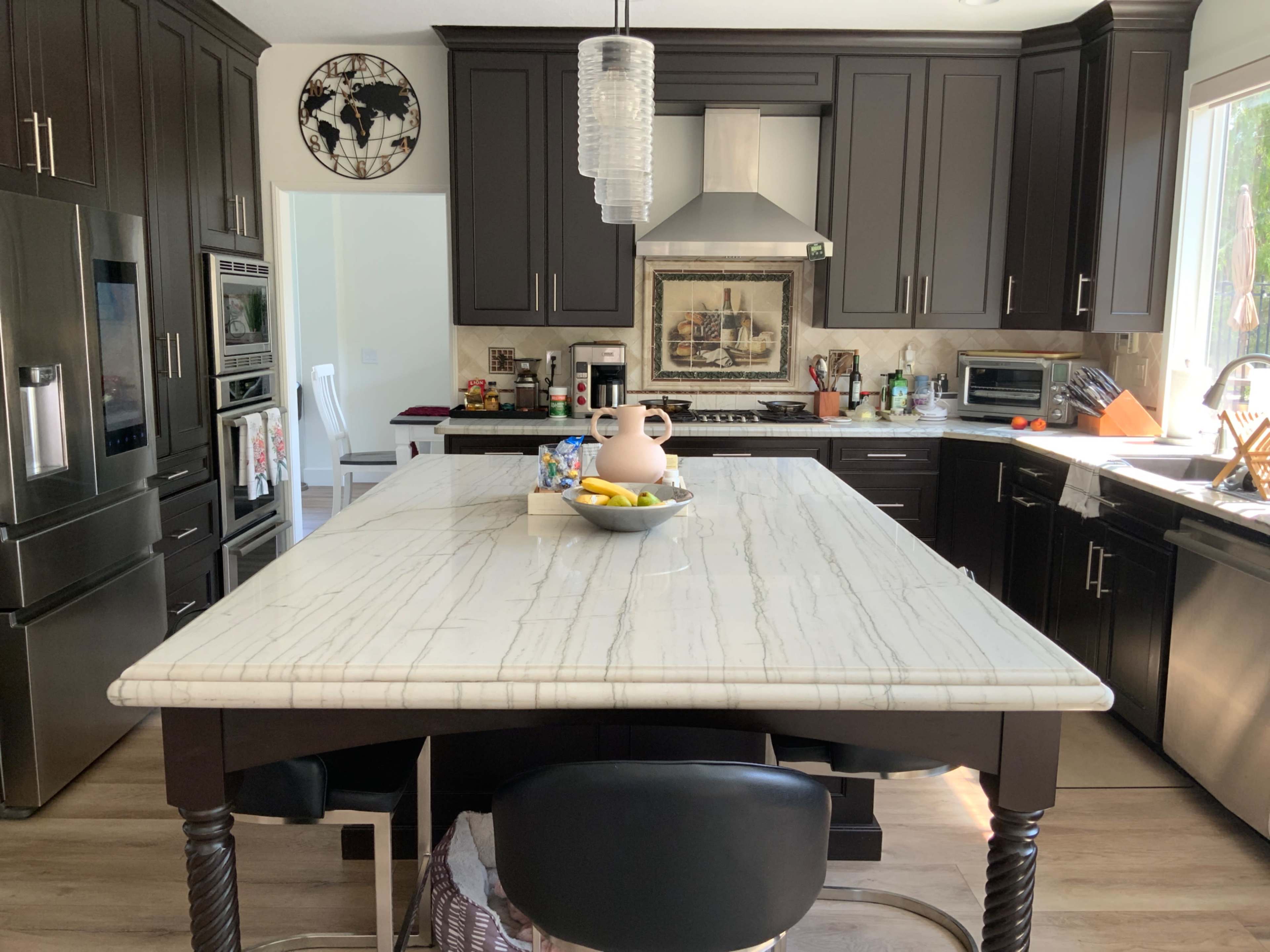 The image shows a modern kitchen with dark cabinetry, a large marble island, and stainless steel appliances.