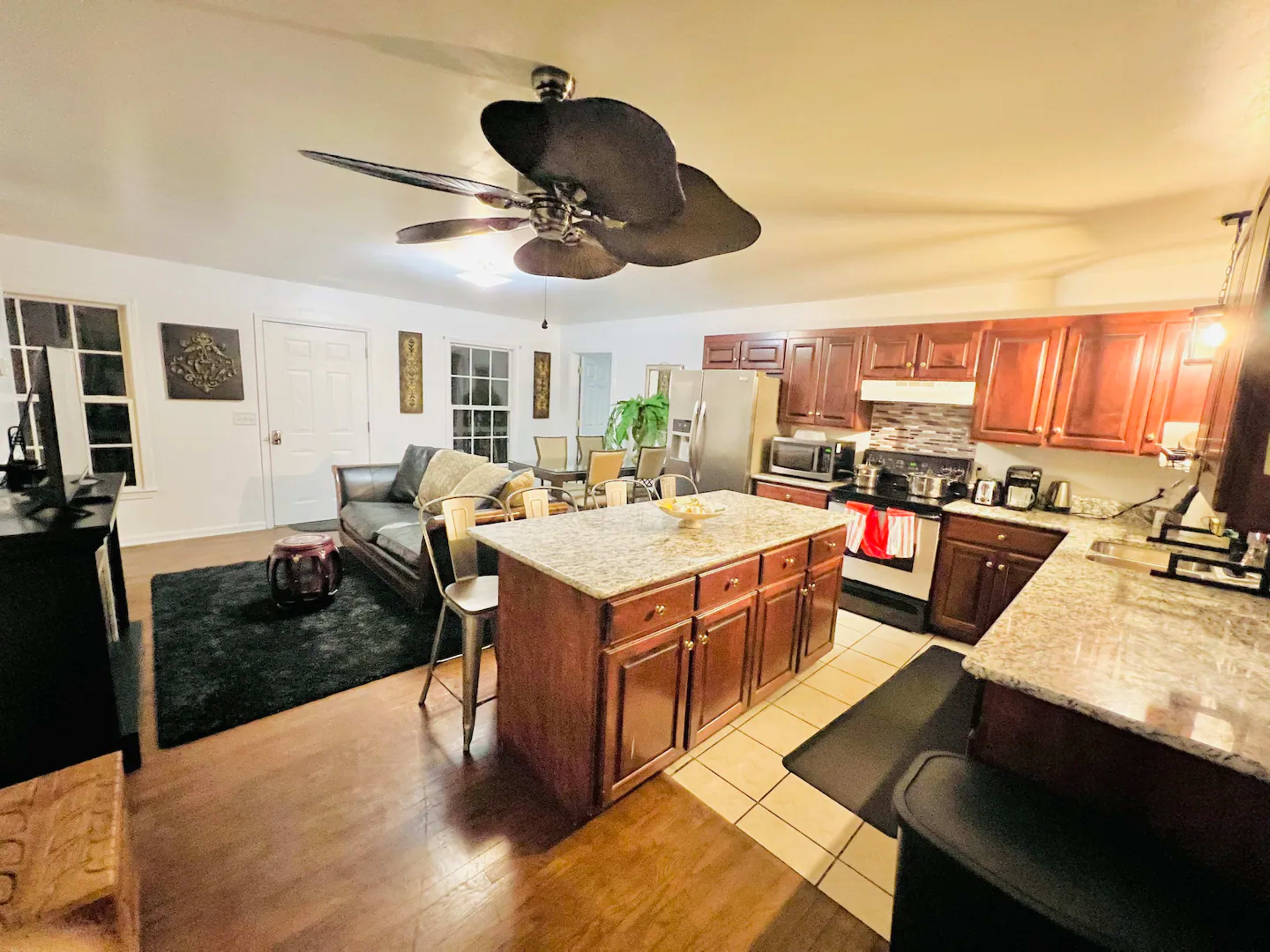 A modern kitchen and living area with wooden cabinets, a granite island, and a seating area with a sofa.